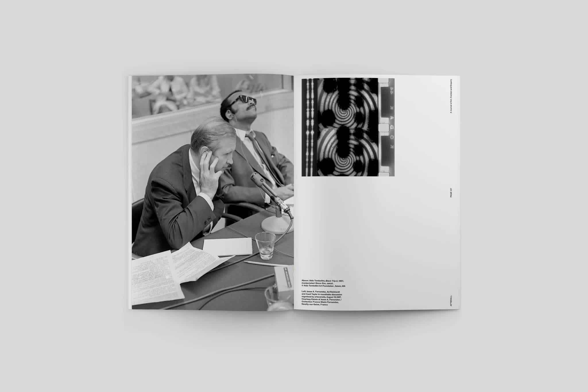 Magazine interior. The left page features a black and white photo of two men sitting at a desk. The right page has a black and white photo in the top left corner and the image credit in the bottom left corner.