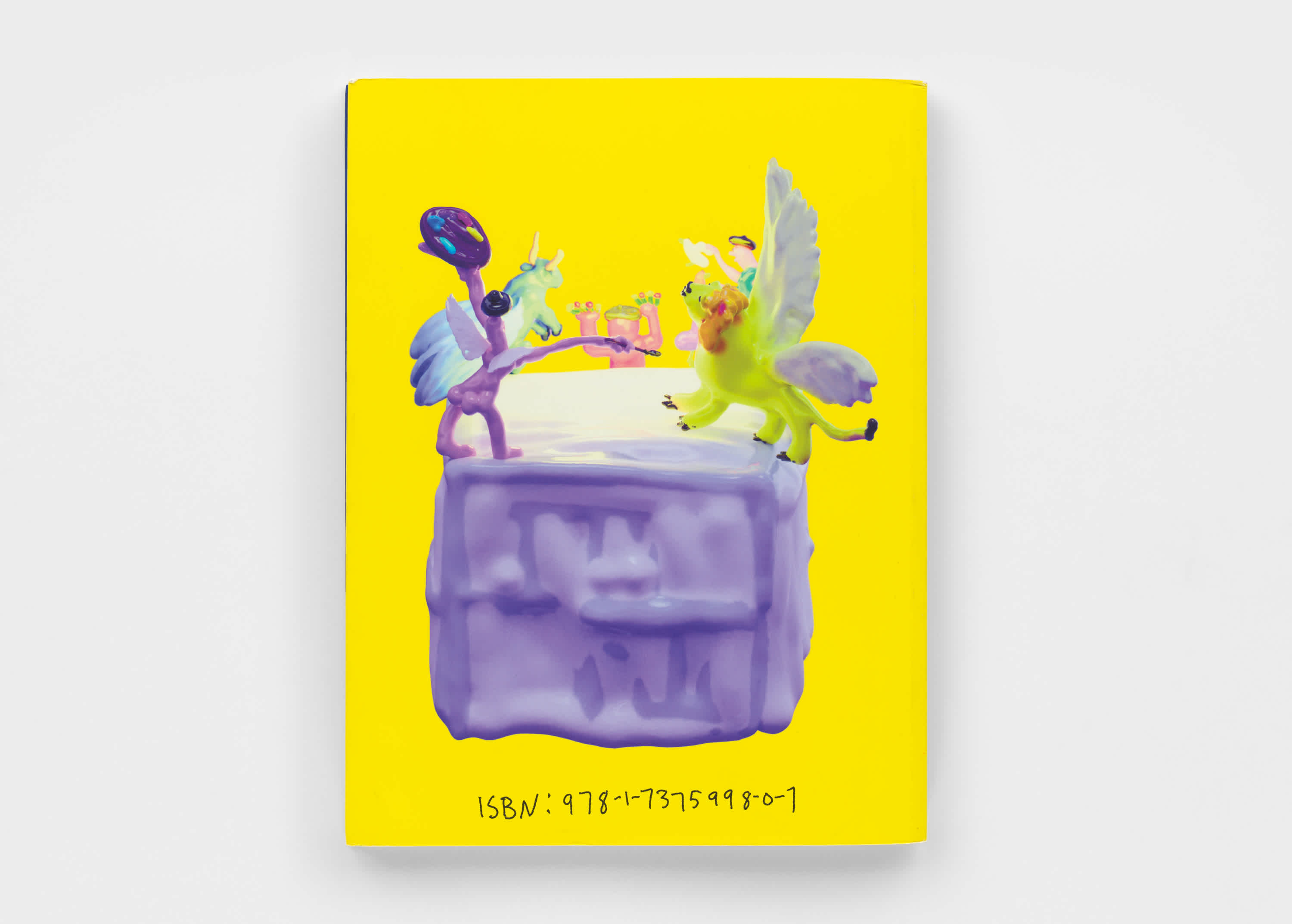 Back cover of a yellow book. A purple, green and pink sculpture is above handwritten text.