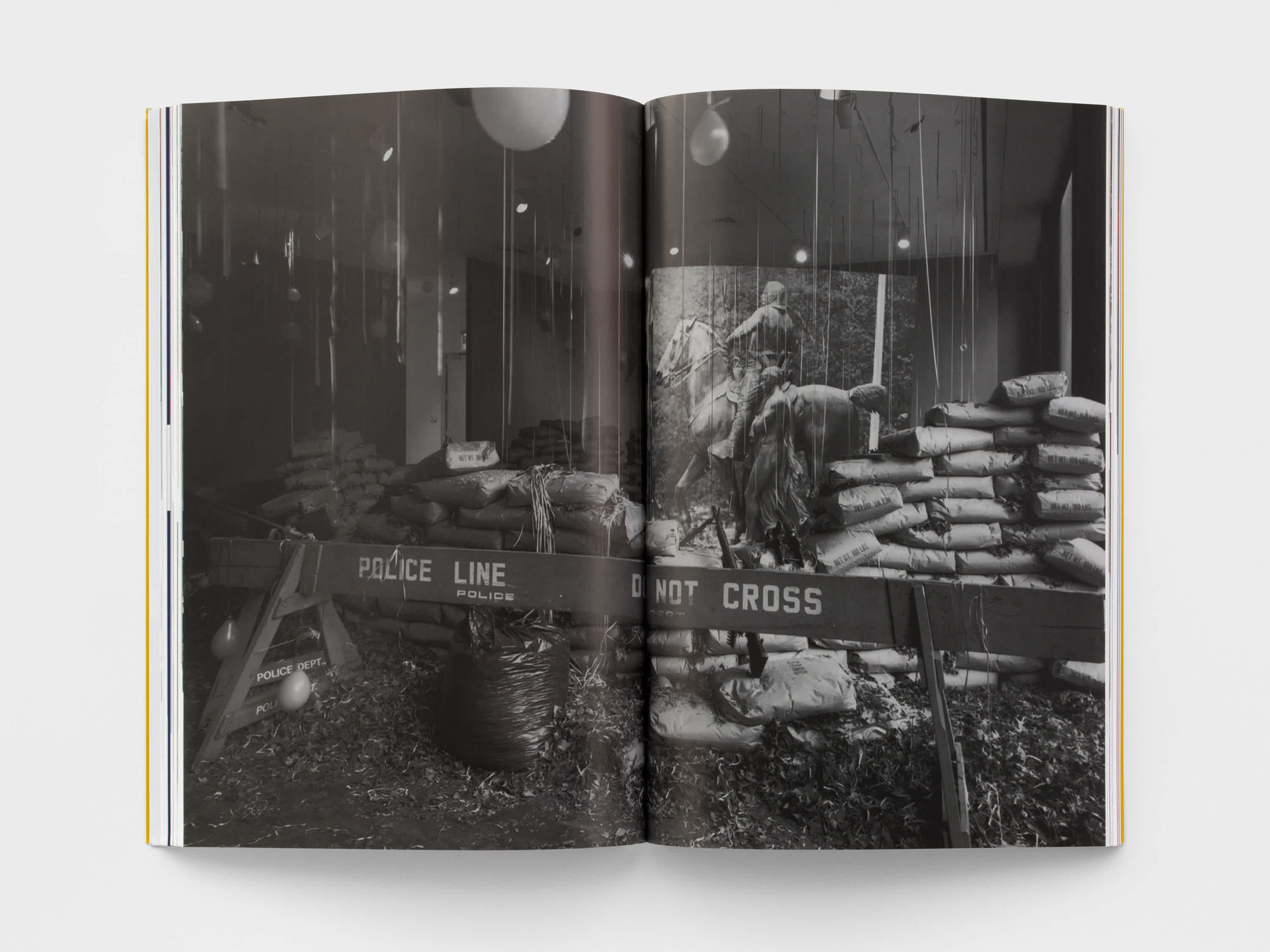 Open magazine with a black and white centerfold of a room filled with balloons, sand bags and a wooden police barricade. 