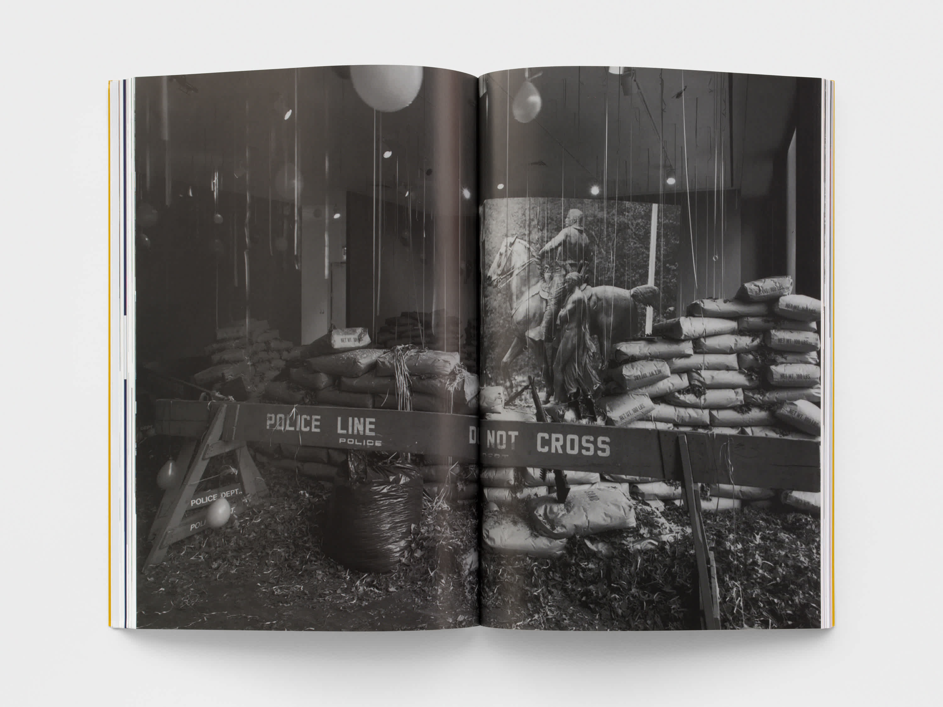Open magazine with a black and white centerfold of a room filled with balloons, sand bags and a wooden police barricade.