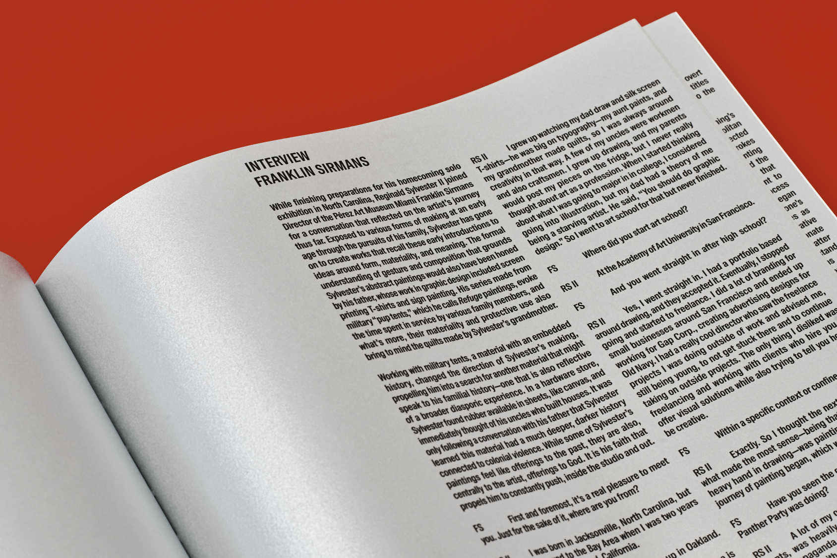 Detail of an open book resting on a red background. The white page features an interview printed in two columns of black text.