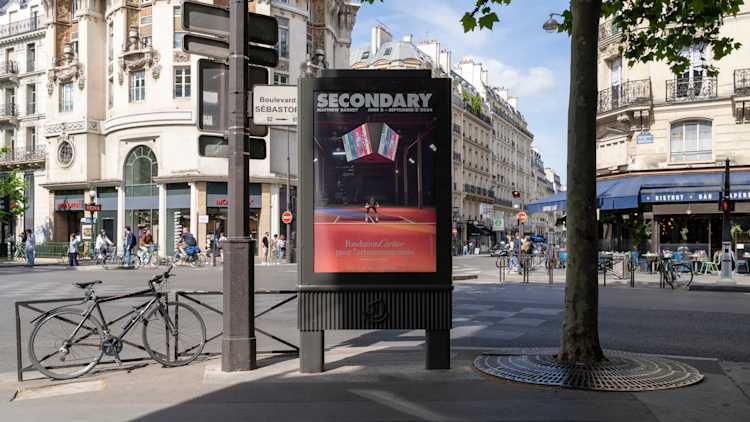 Image of a poster on the street in Paris. The poster features a man in a football uniform below a jumbotron with the word "Secondary" at the top of the poster.