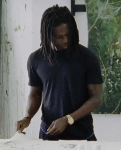 Artist wearing black t-shirt and gold watch flips through a catalogue of his work in front of a green painting.