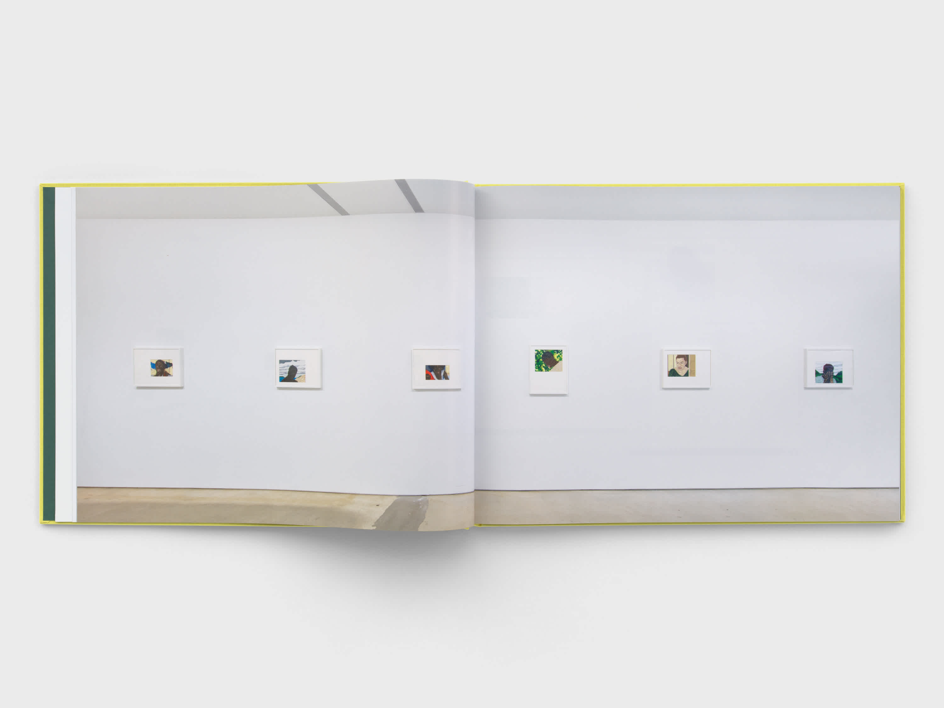 Book centerfold that shows a photograph of a wall from an exhibition. The wall is white and six small drawings hang on it.  