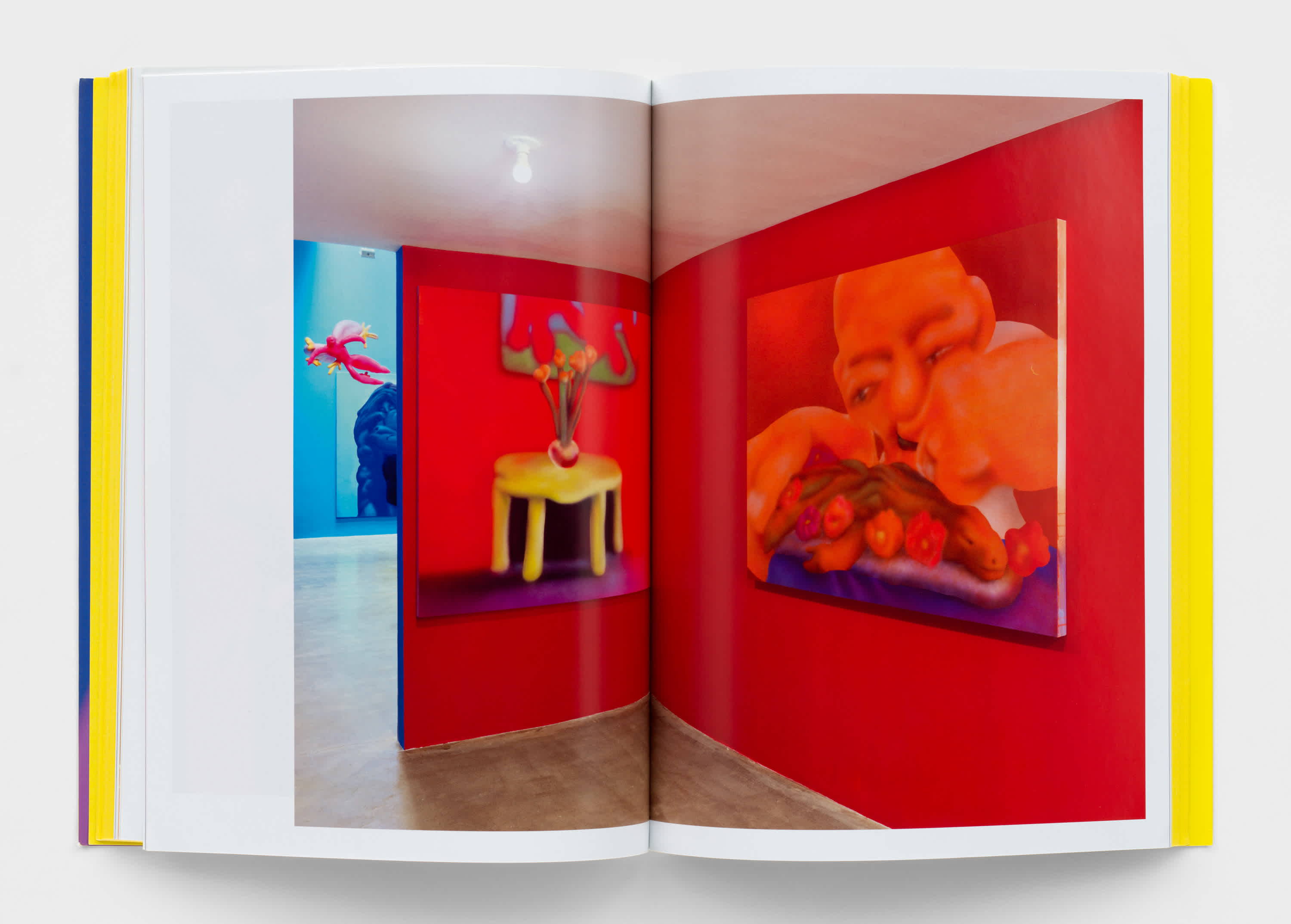 Book interior with a centerfold image of a painting exhibition. Two paintings hang on a red wall in the foreground. In the background a sliver of a painting on a blue wall sticks out. 
