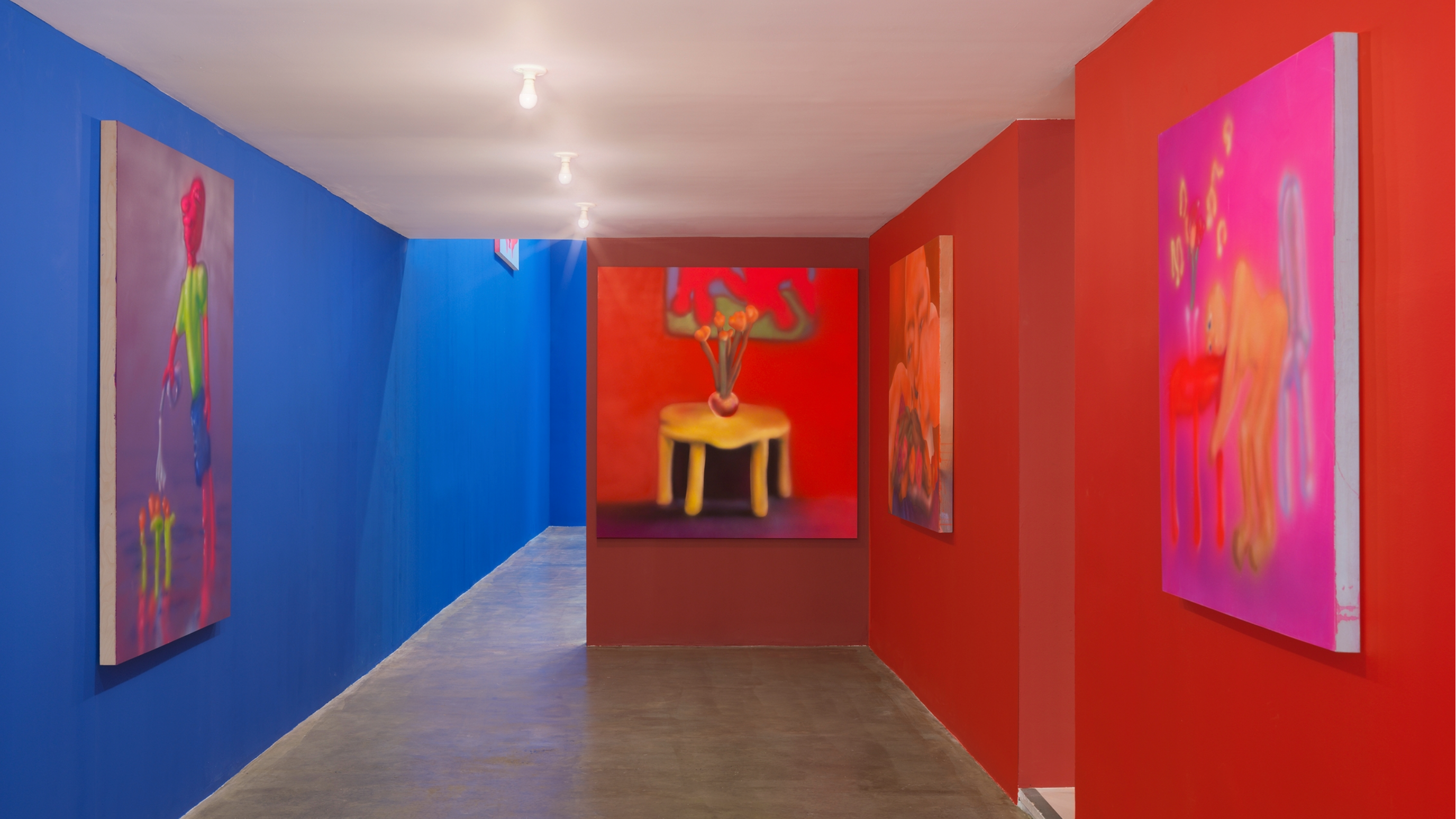 A room of red and blue walls. Four colorful paintings hang on the walls.