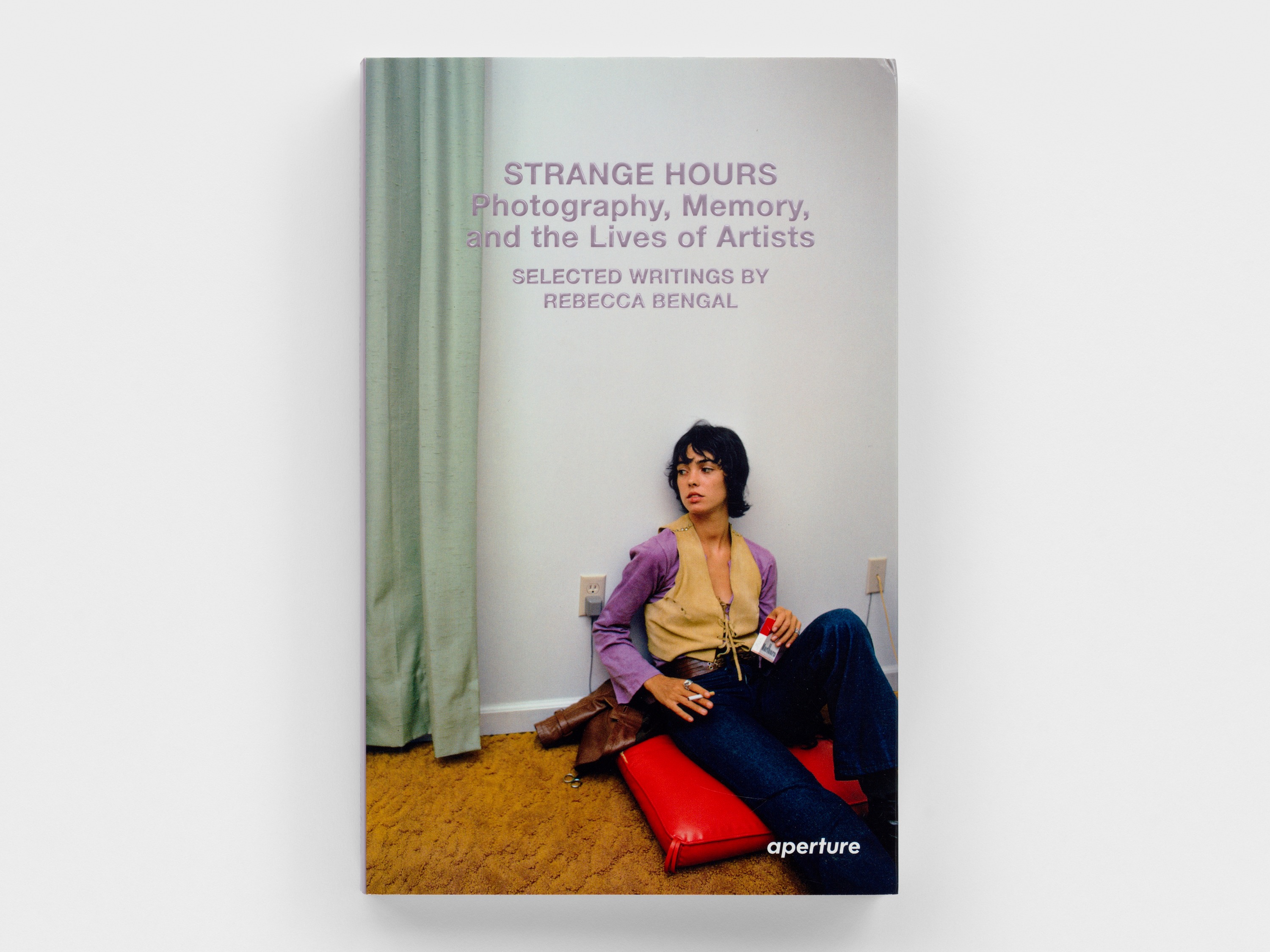 Book cover with purple text over a color photograph of a woman seated on the floor smoking a cigarette.