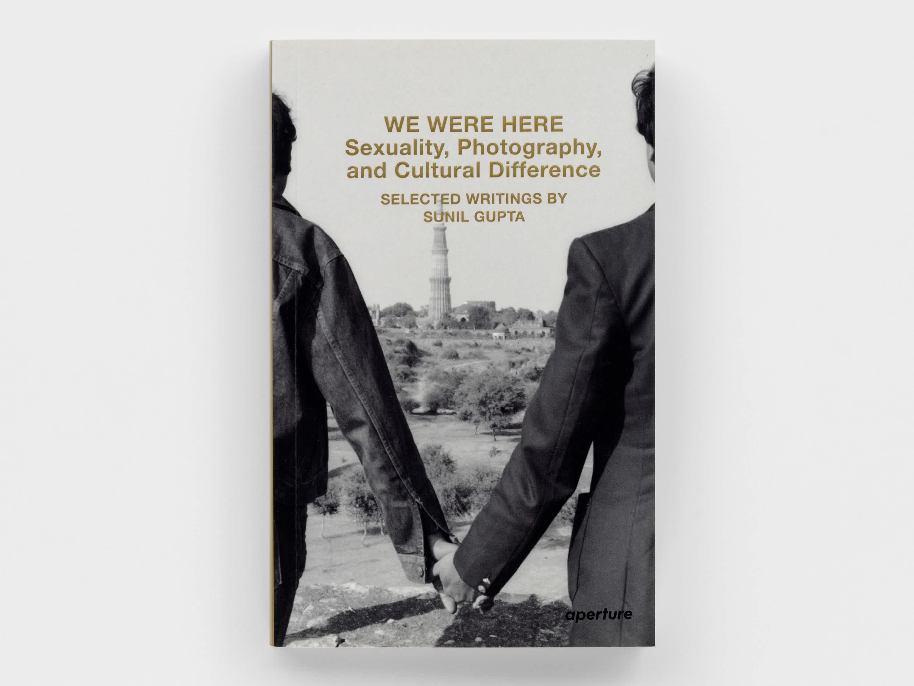 Book front cover of two men holding hands. Only their clasped hands and shoulders are visible. They look out at the horizon. The title and author of the book are embossed in matte gold just above the two men's shoulders. 