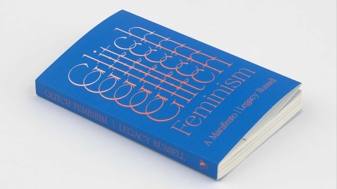 Dark blue book laying flat so the front cover and spine are visible. The word "Glitch" slides from top to bottom in a repeating pattern. The word "Feminism" is just below this followed by "A Manifesto" and the author, Legacy Russell's name. The text is printed in a white to peach gradient.