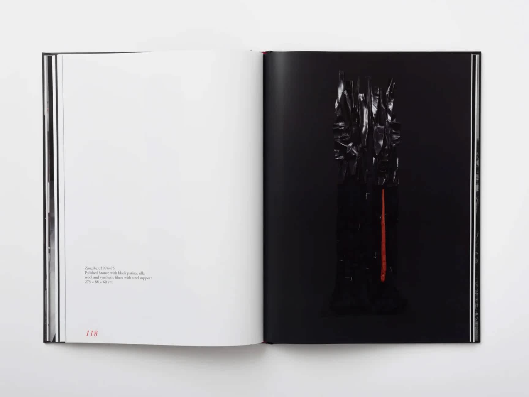 An open book in which the left page is white and the right page features a black metal sculpture in a black room.