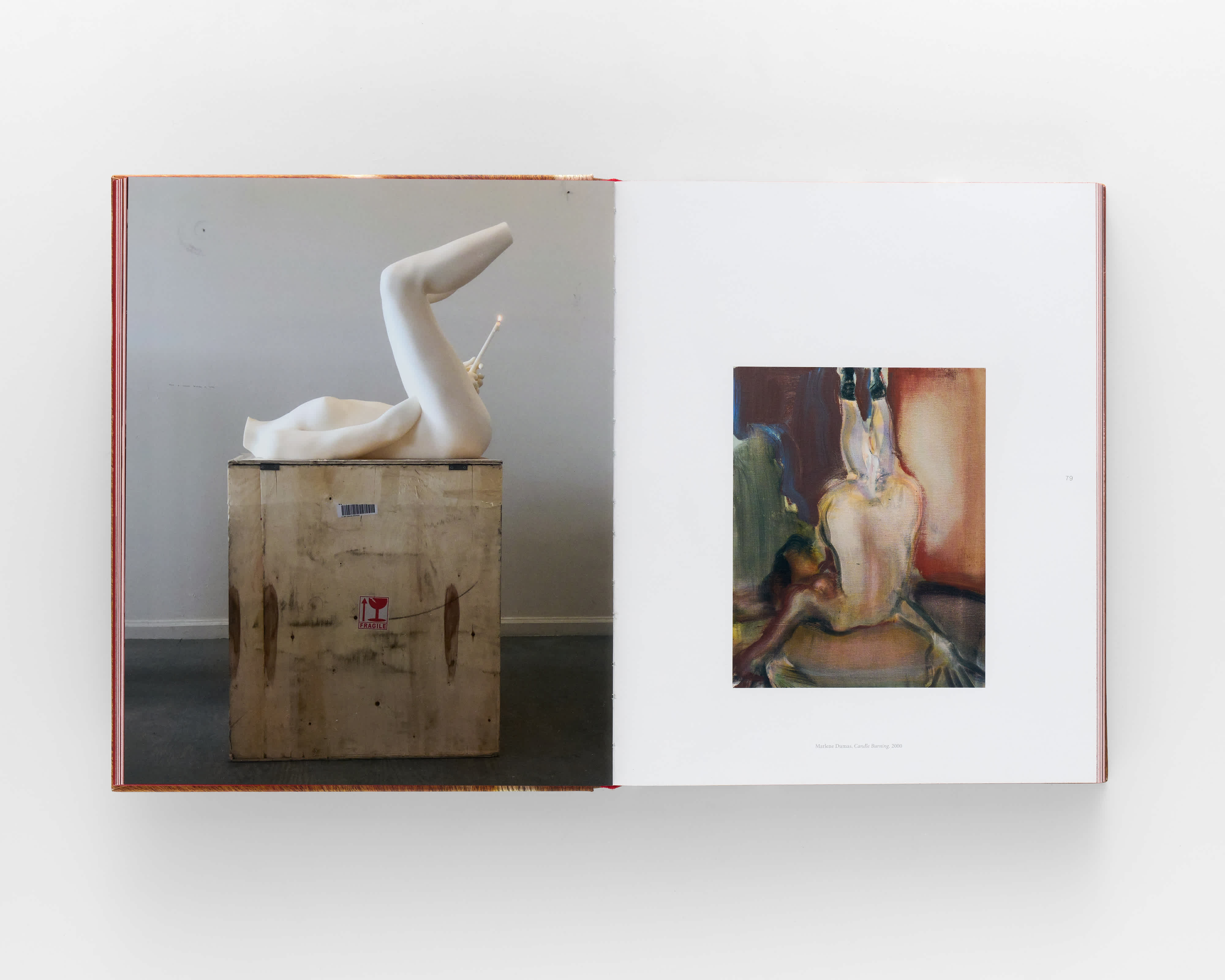 An open book on a grey background. The left page features a sculpture of a human body positioned on top of a shipping crate. The body has its legs raised in the air and holds a candle at its genitals. 

The right page features a painting by Marlene Dumas titled 'Candle Burning' in which a figure lays on its back, legs in the air. 