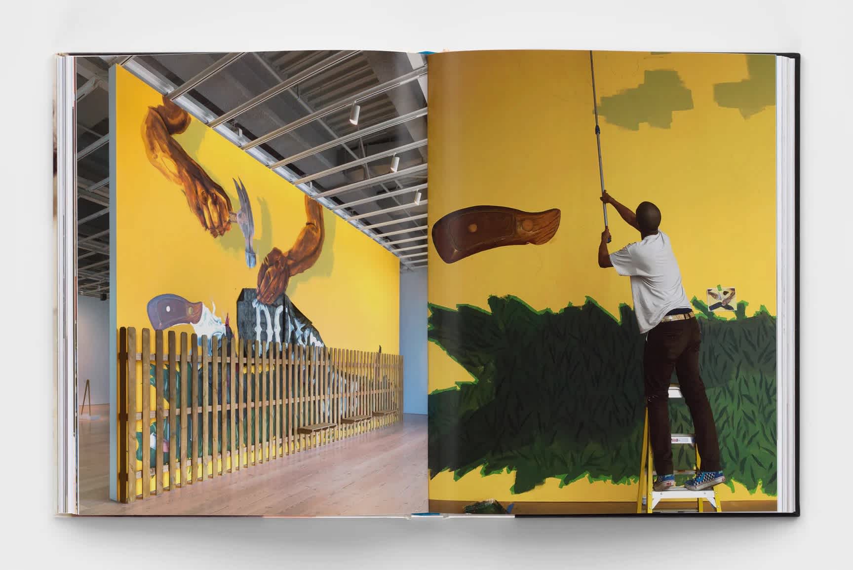 Open book which features an installation shot of a yellow, green and brown mural in a gallery space. The opposite page is a photograph of the artist installing the artwork.