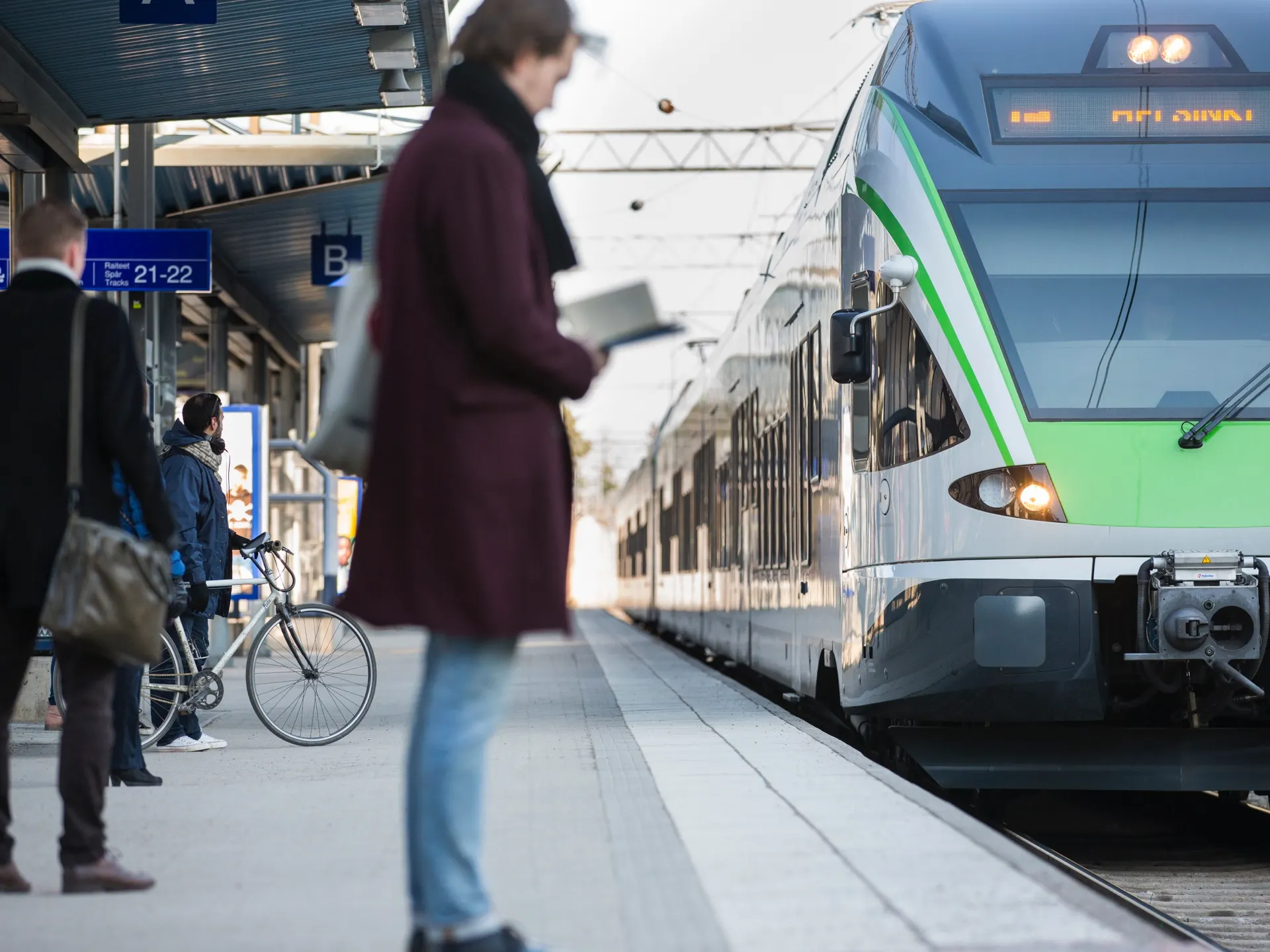 A commuter train arrives at the platform, and passengers are standing on the platform waiting to board the train.