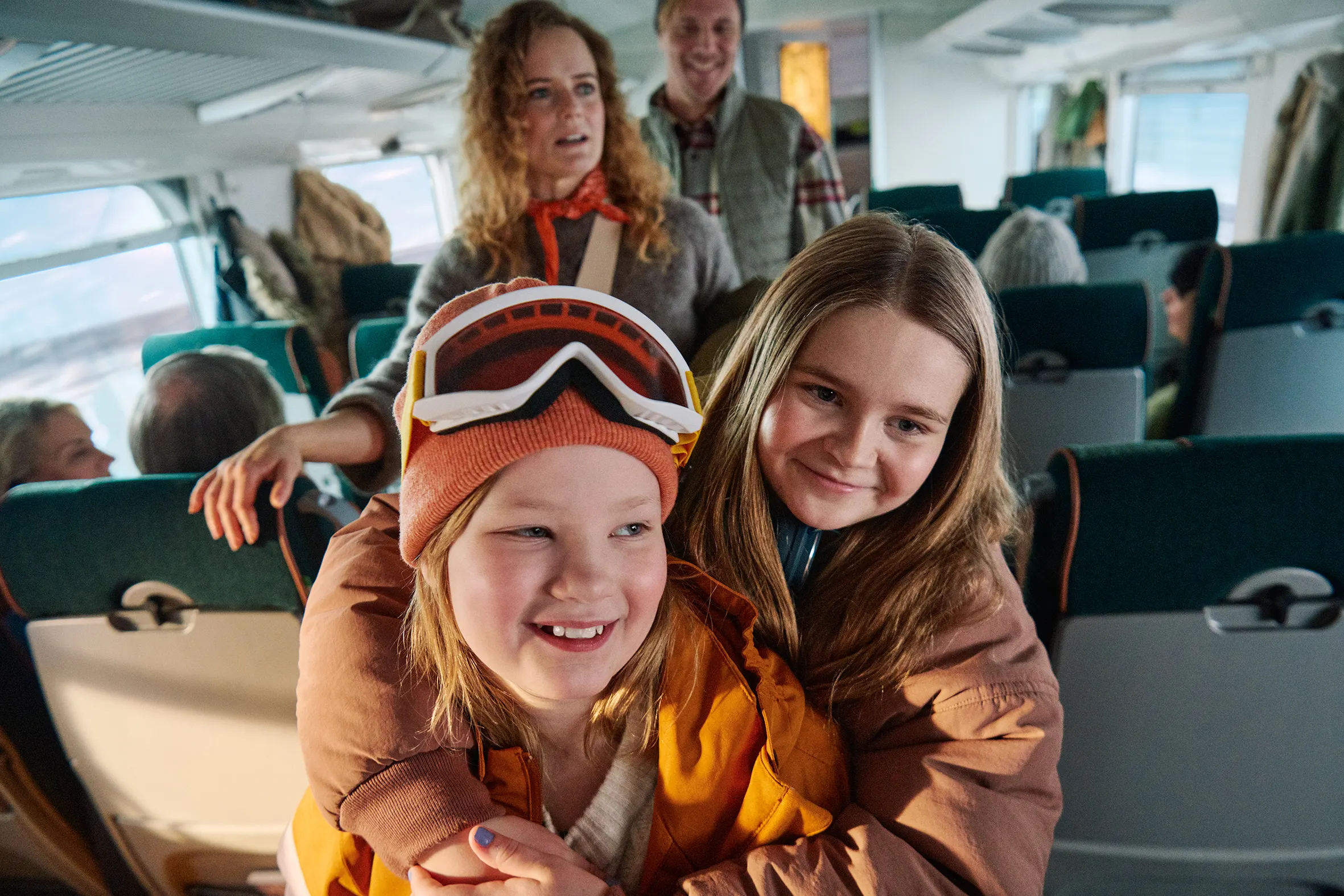 Kvinna som ler på tåget med mössa på huvudet och skidor i handen.