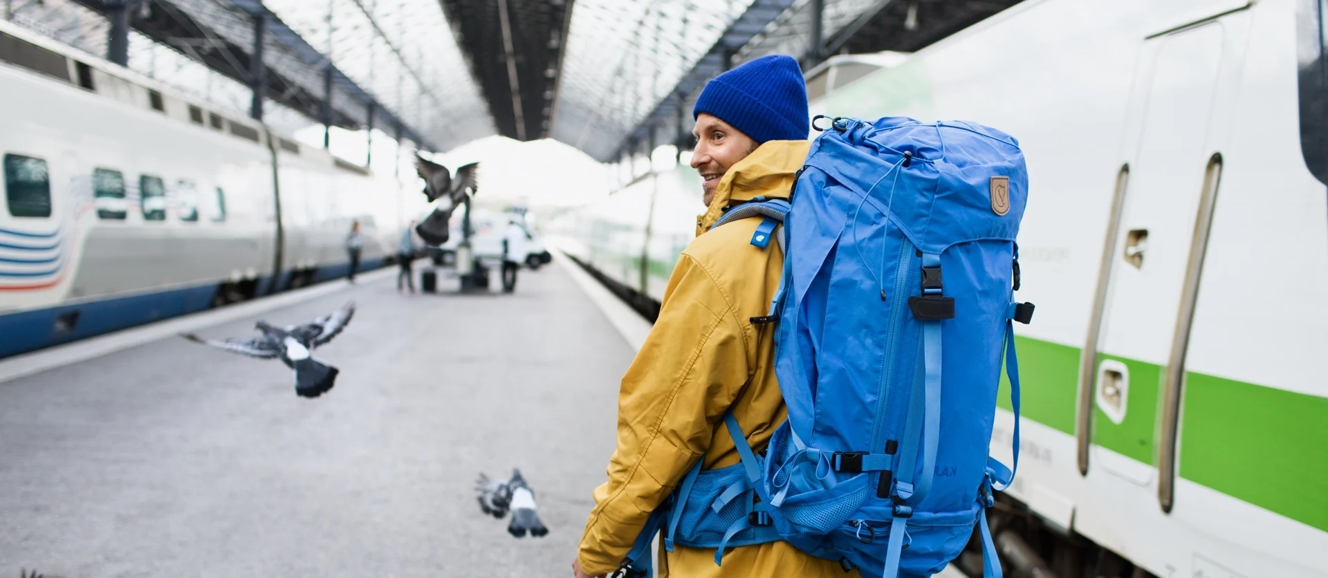 A passenger is walking with a large backpack on a railway station platform. 