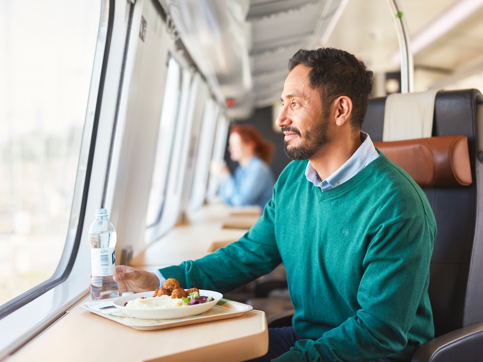 Matkustaja syö lounasta junan ravintolavaunun yläkerran yksittäisellä paikalla ja katselee maisemia.