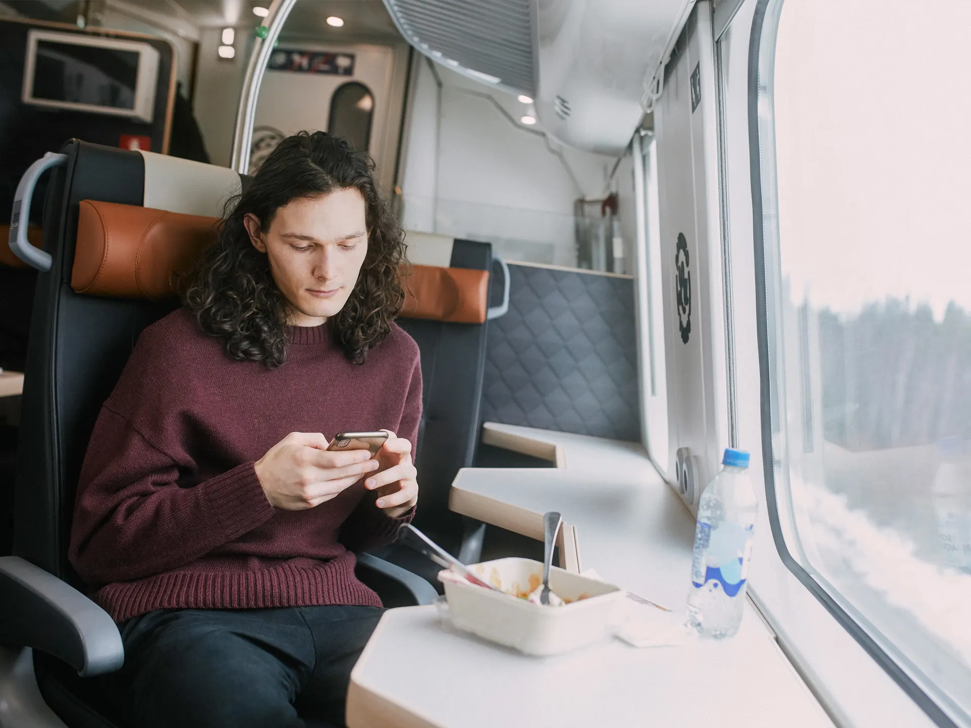 Matkustaja syö lounasta junan ravintolavaunun yläkerran yksittäisellä paikalla ja katselee maisemia.