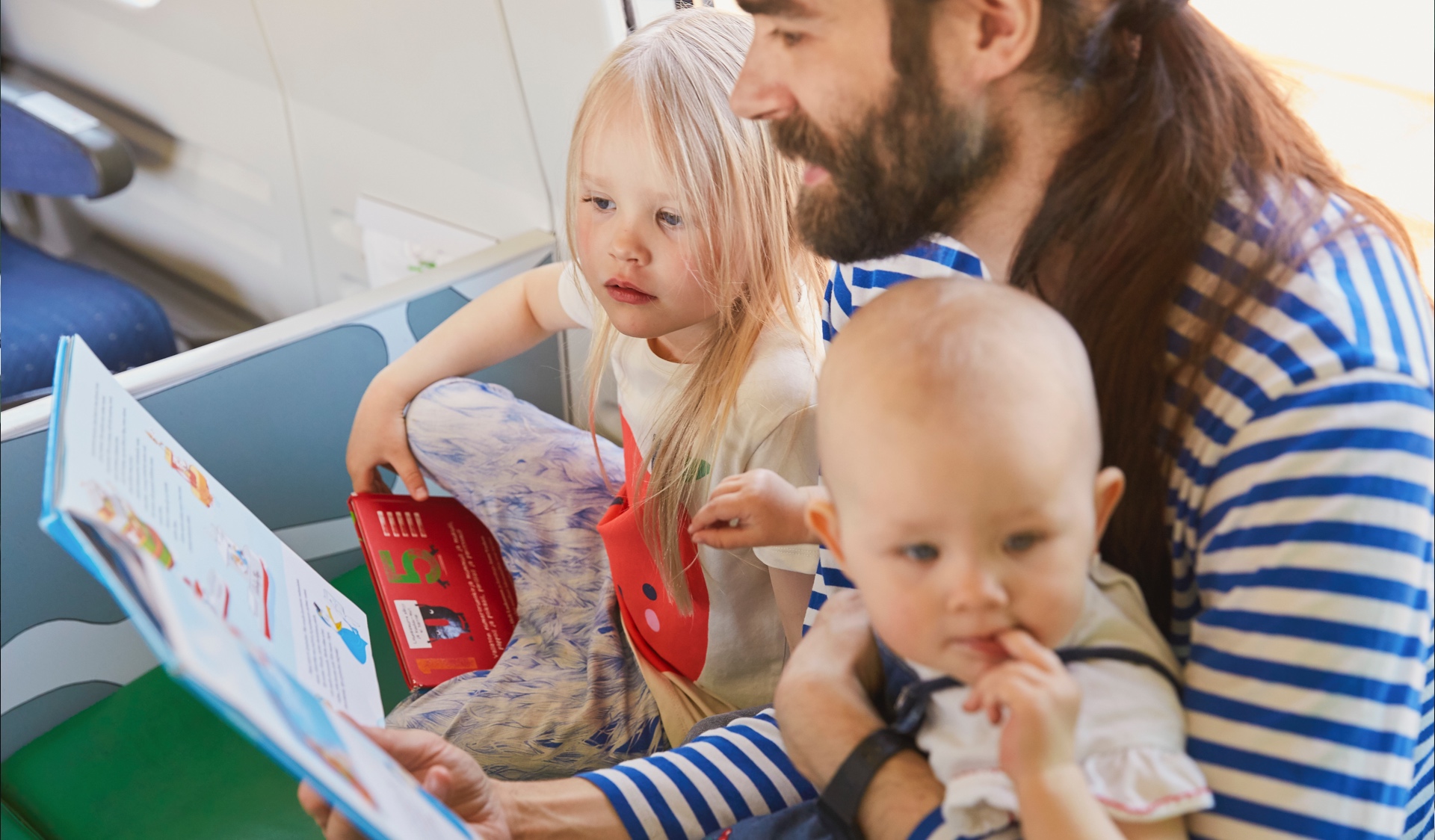 En pappa läser en bok högt för två barn i lekhörnan på tåget.