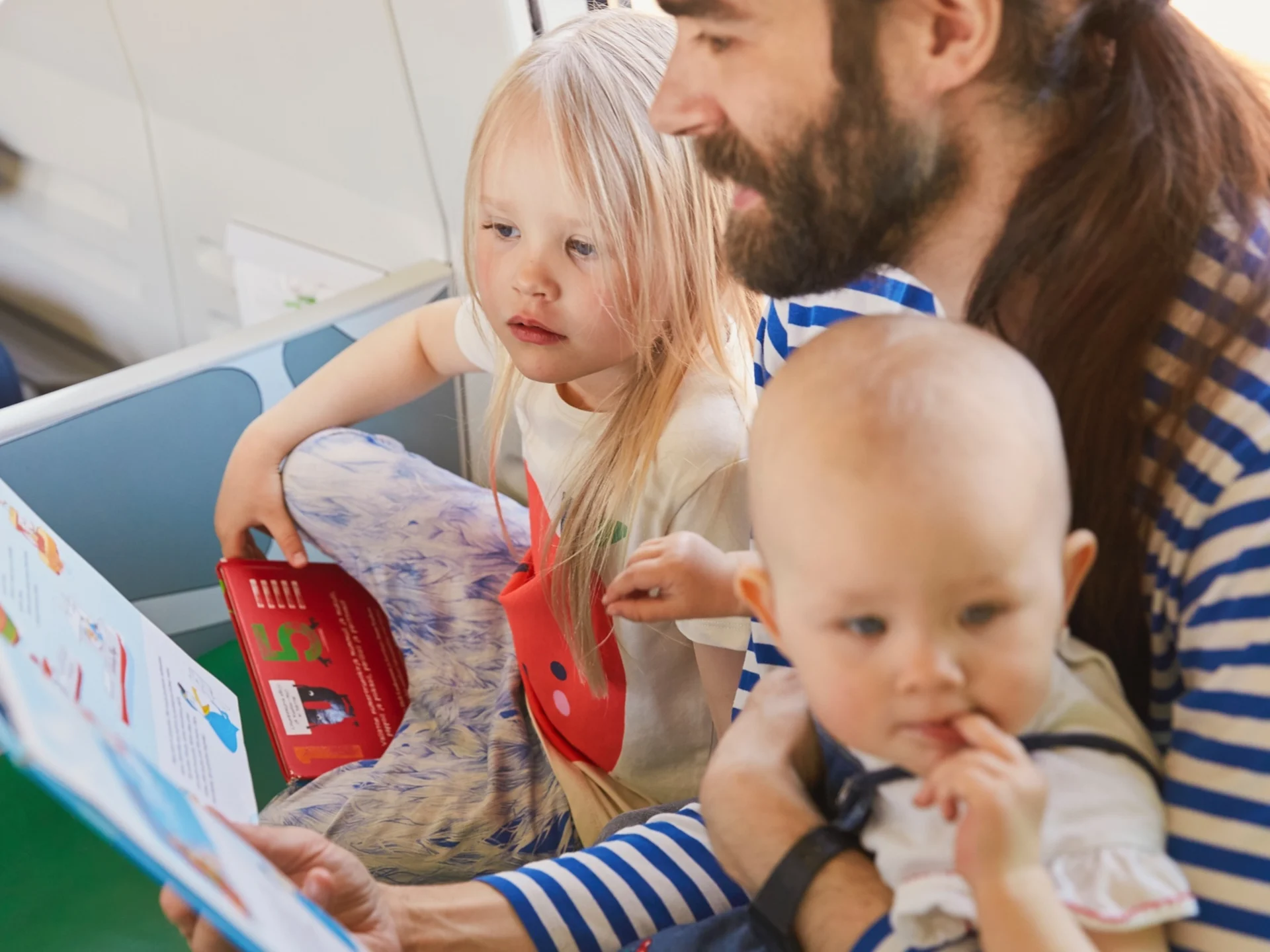 Isä lukee kirjaa kahdelle lapselle junan leikkipaikalla.