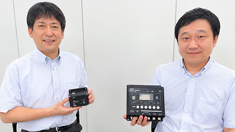 オムロンのIP67・パワーサプライを手に持ち笑顔で並んで座る、商品開発を推進したコンポ事業部の澤井氏(左)と鷹取氏(右)