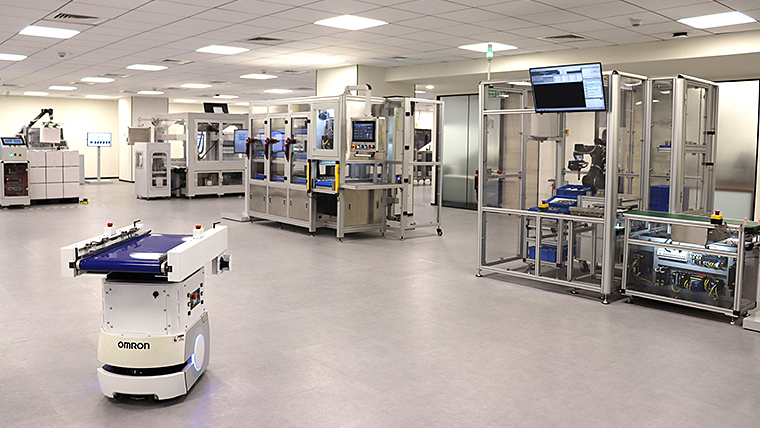 Interior view of the OMRON Automation Centre in Bengaluru, featuring advanced automated manufacturing systems and a mobile robot in the foreground.