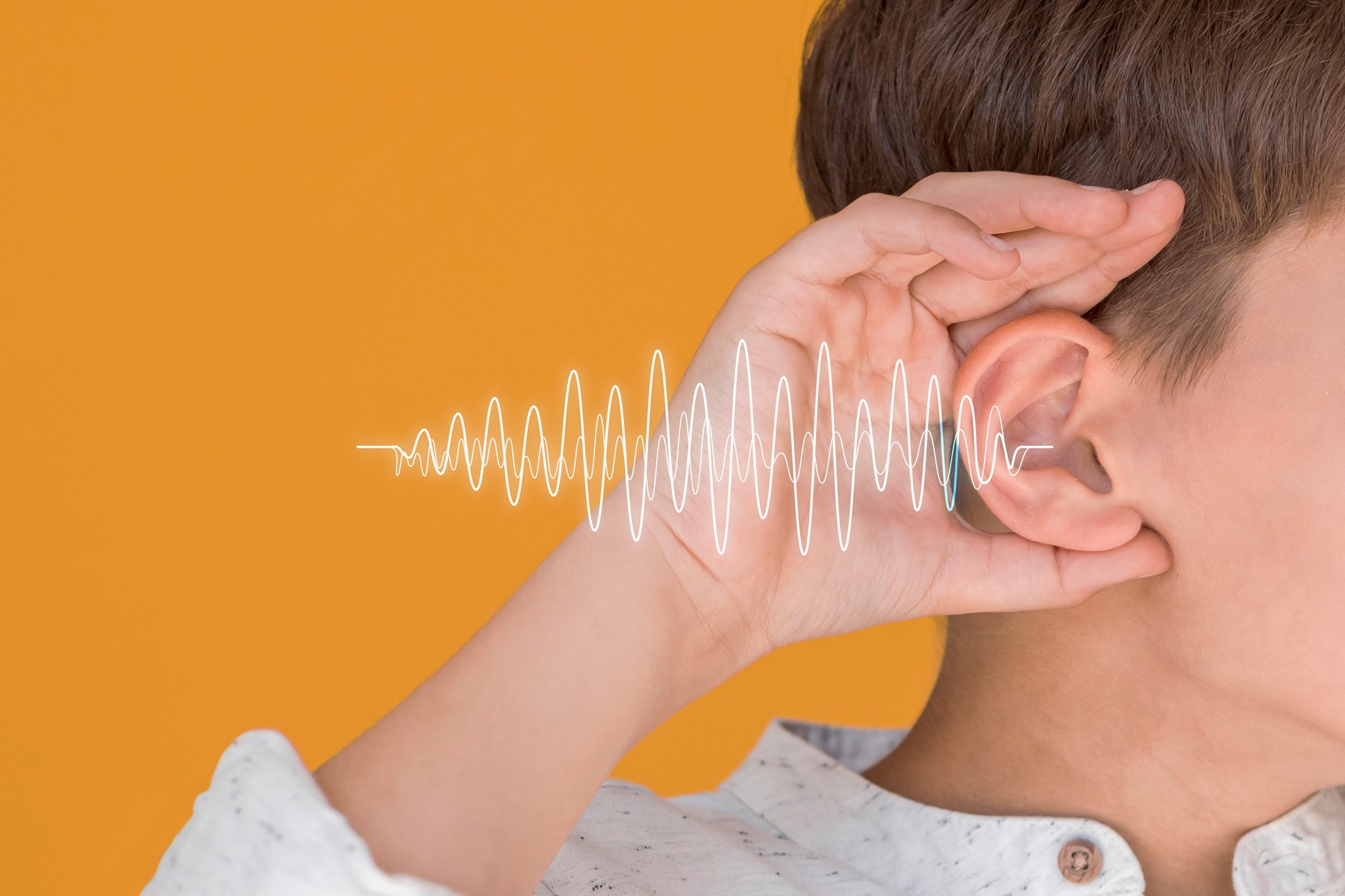 Un niño con la mano derecha en su oreja y a un lado un dibujo de ondas que simulan sonido