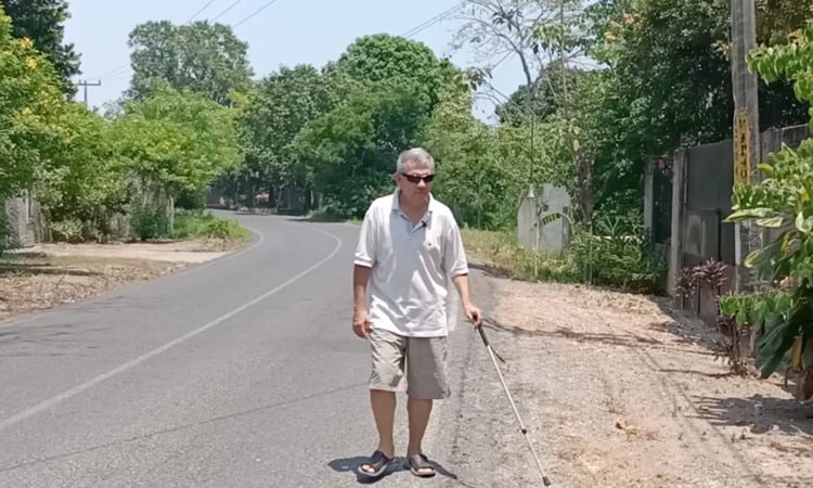 Enrique Guzmán caminando por la calle con un bastón y usando lentes oscuros.