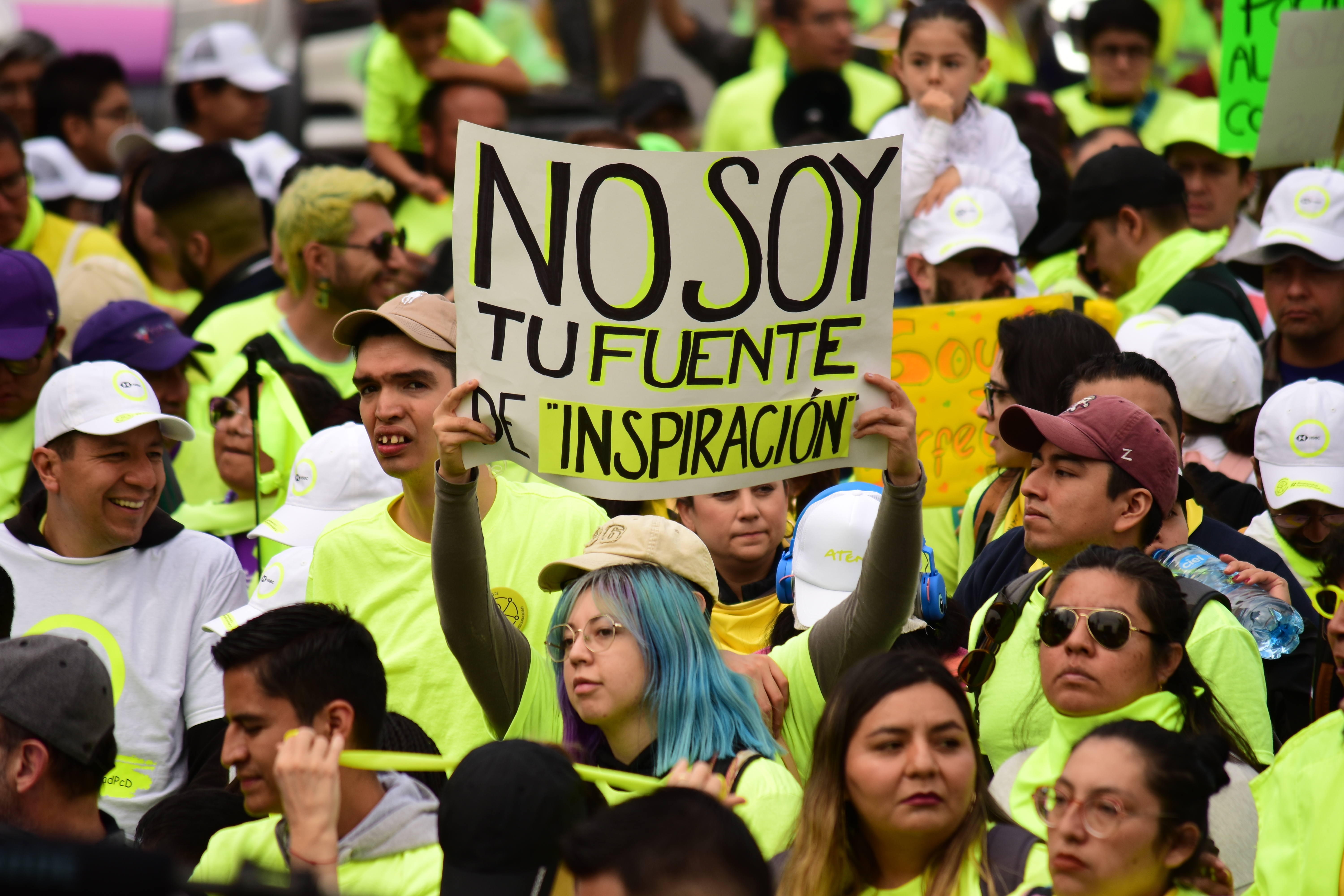 Personas vestidas de amarillo fosforescente una de ellas levanta una pancarta que dice: "No soy tu fuente de inspiración".