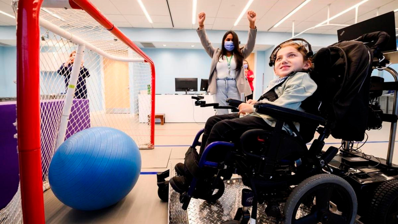 Niña en silla de ruedas usando en su cabeza una diadema que incluye la Interfaz Cerebro-Computadora, frente a una pelota y una portería.