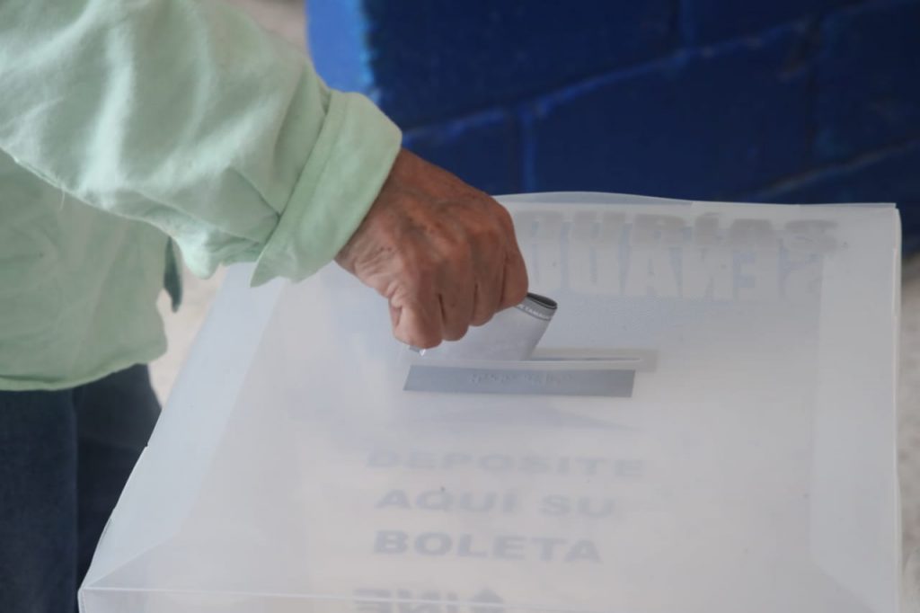 Mano de una persona metiendo su voto en una urna.