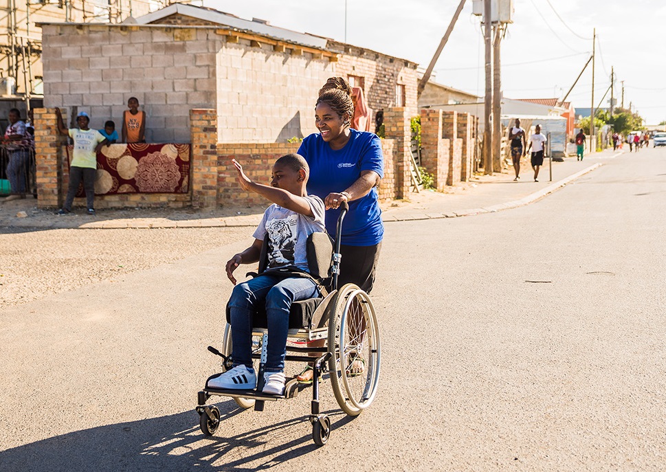 Un joven en silla de ruedas acompañado por una mujer © Shonaquip Social Enterprise
