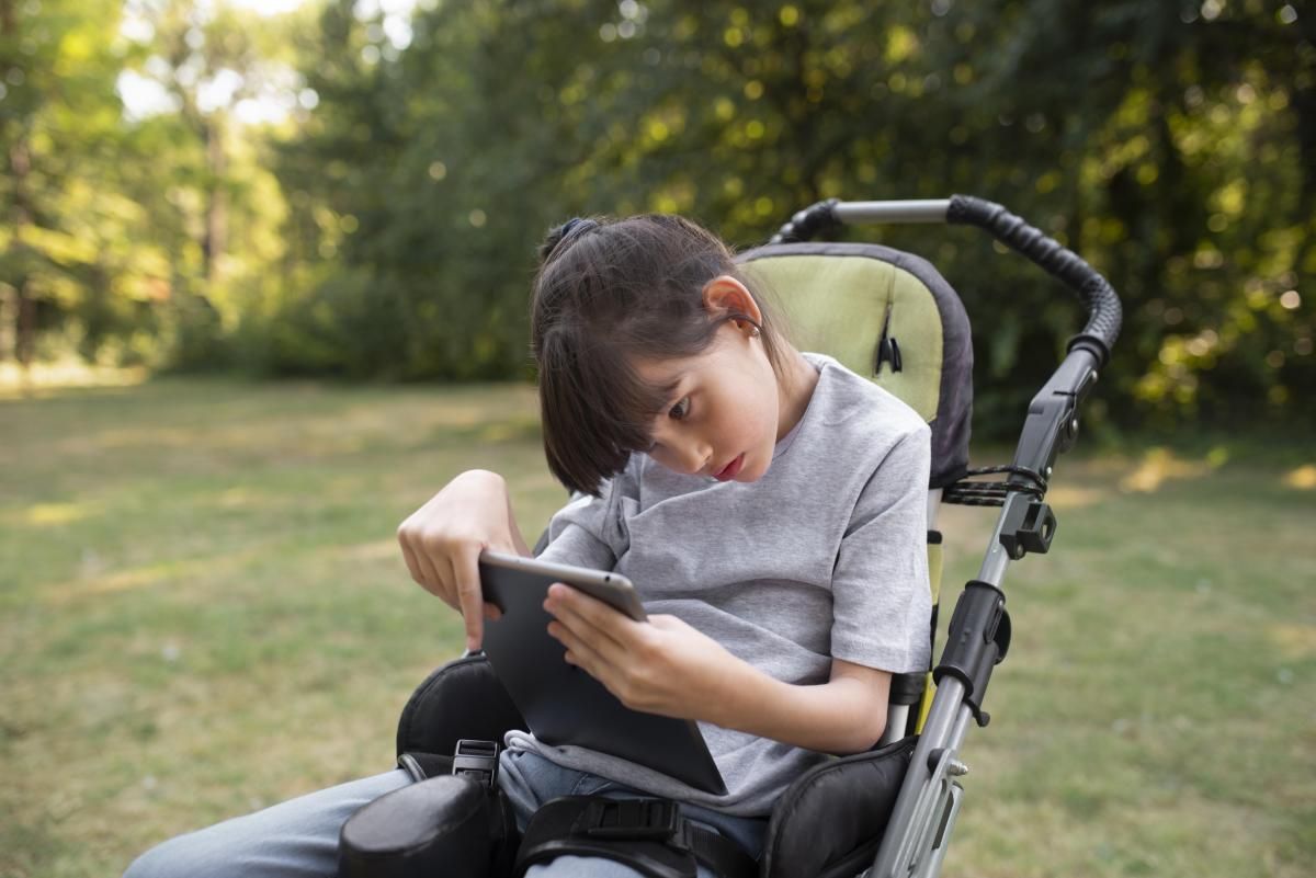 Una chica con parálisis cerebral sosteniendo una tableta y sentada en su silla

