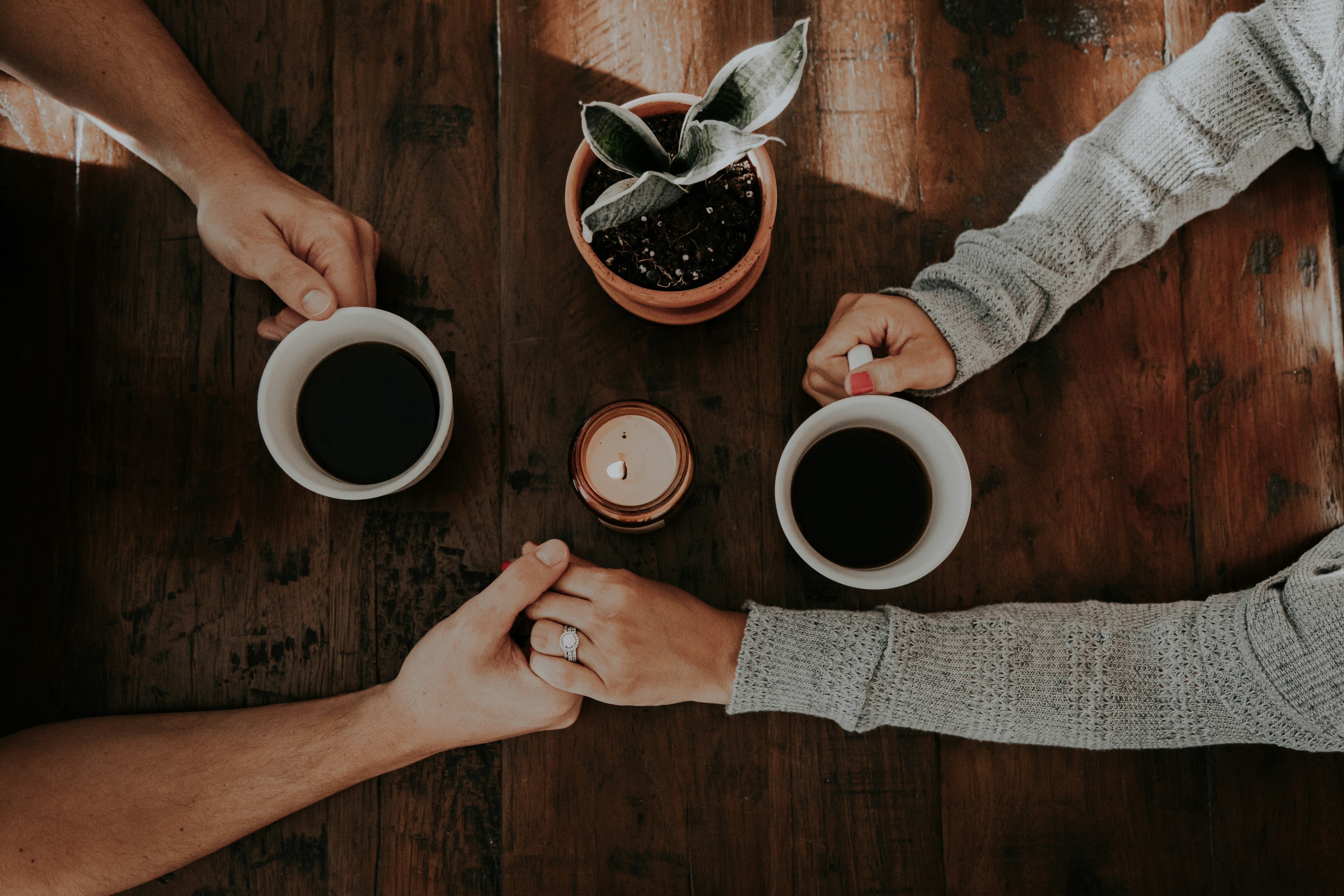 Dos personas sosteniendo su mano mientras con la otra agarran una taza de café.