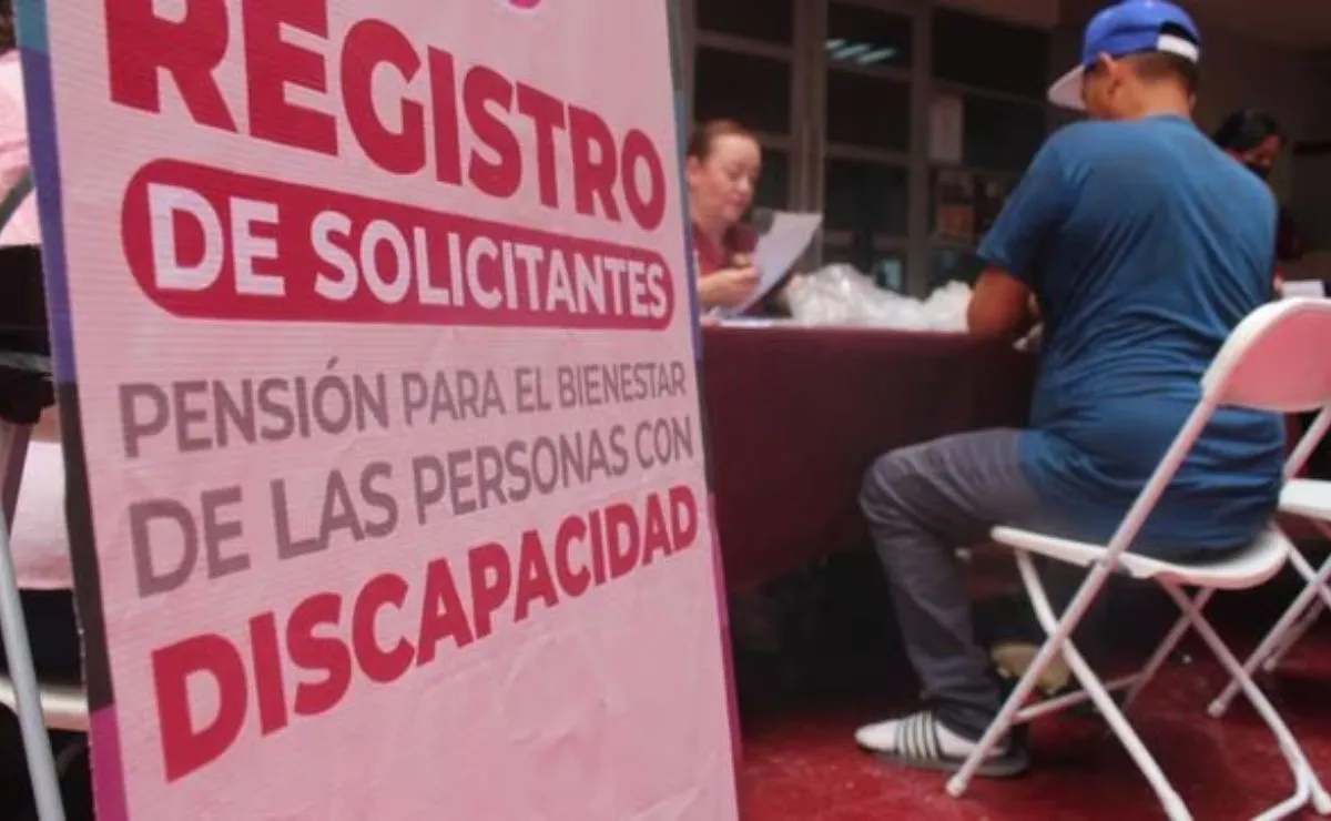 Hombre sentado. Delante de él un cartel en el que se lee: Registro de solicitantes Pensión para el Bienestar de las personas con discapacidad.