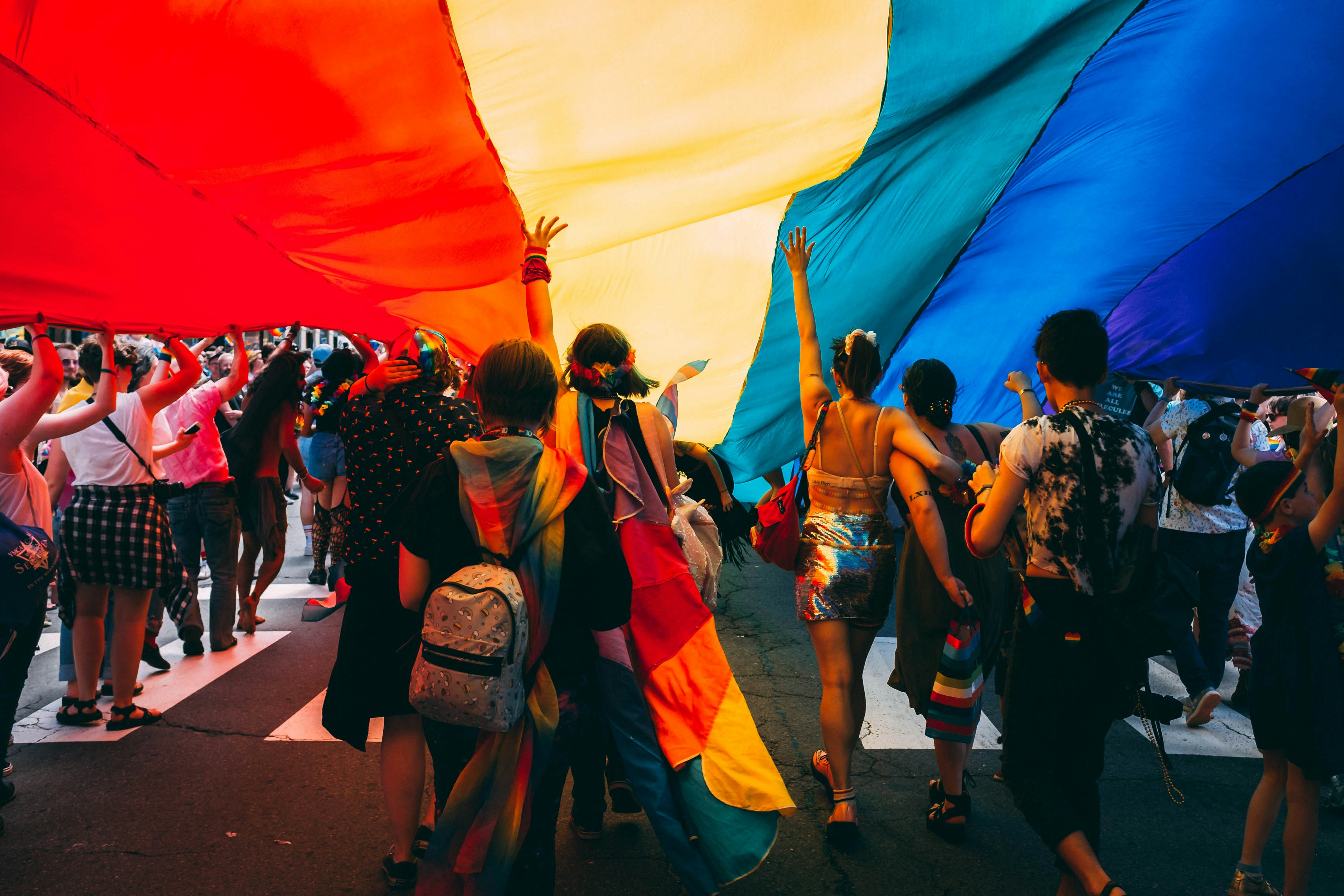 Conjunto de jóvenes sosteniendo una bandera LGBTTTIQ en una marcha.