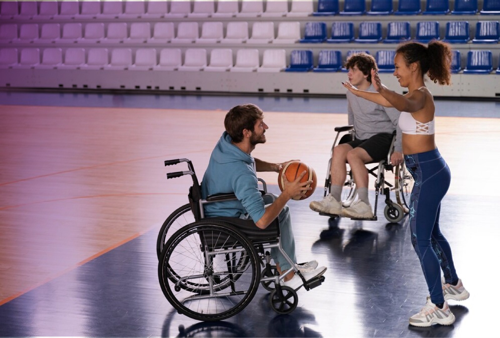 Dos jóvenes en silla de ruedas jugando baloncesto con una mujer.