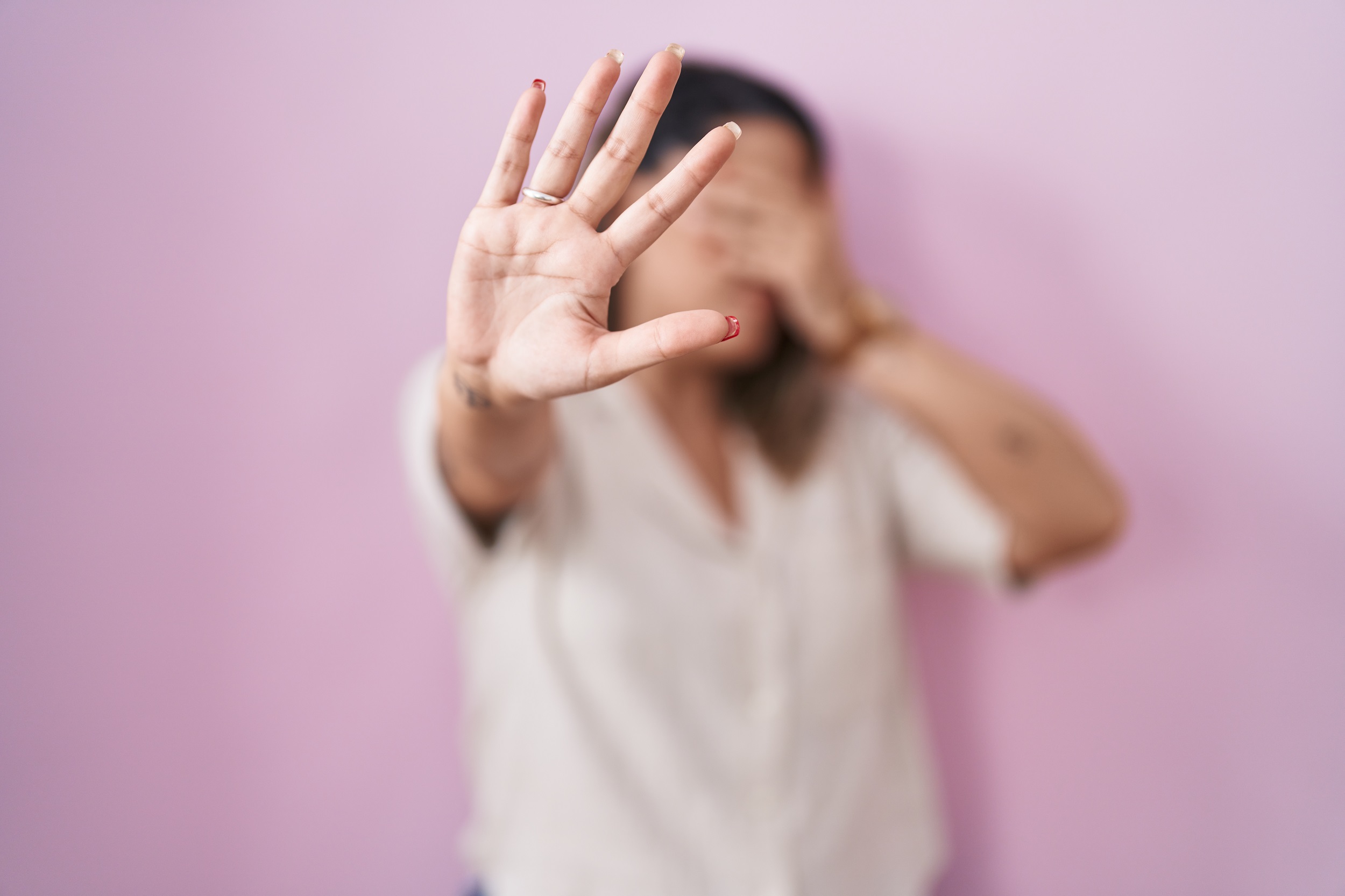 Una mujer cubriéndose el rostro, con el brazo extendido y mostrando la palma de su mano en señal de basta.