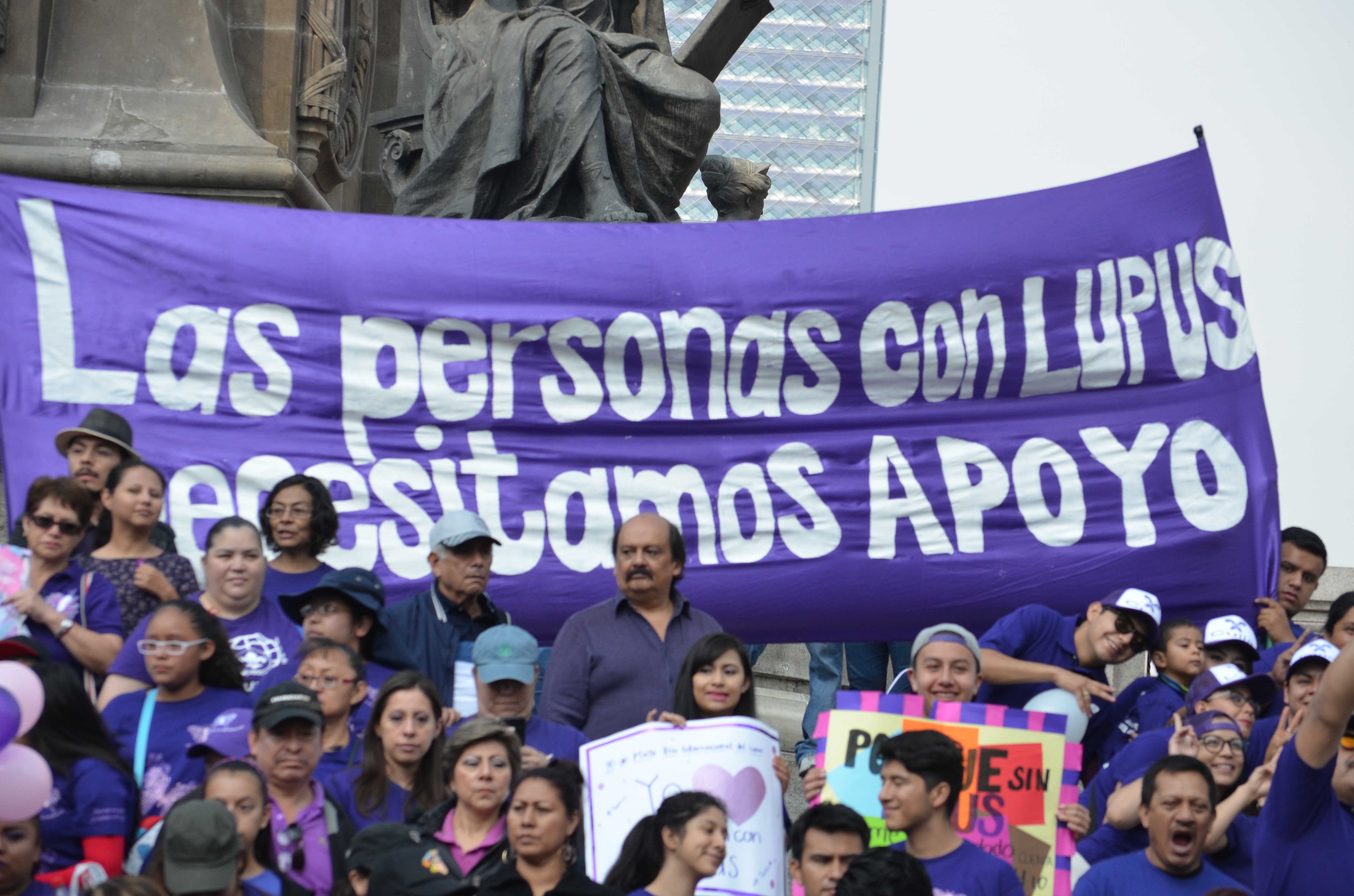 Grupo de manifestantes vestidos de morado frente a un cartel que dice Las personas con Lupus necesitamos apoyo.