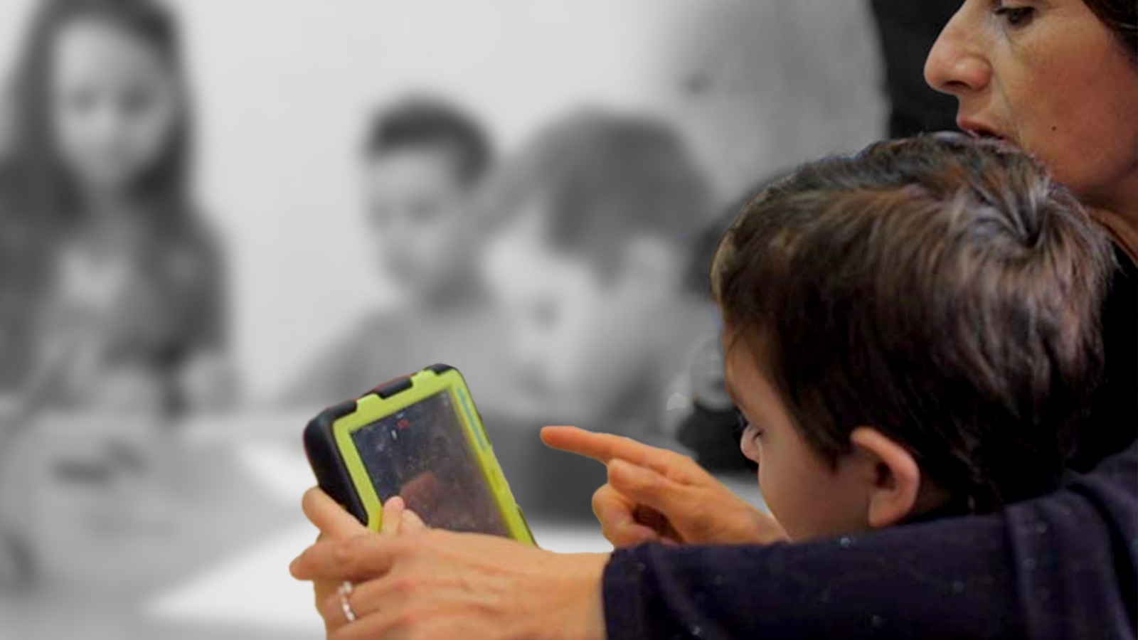Maestra sentada al lado de un niño que está frente a una tableta.