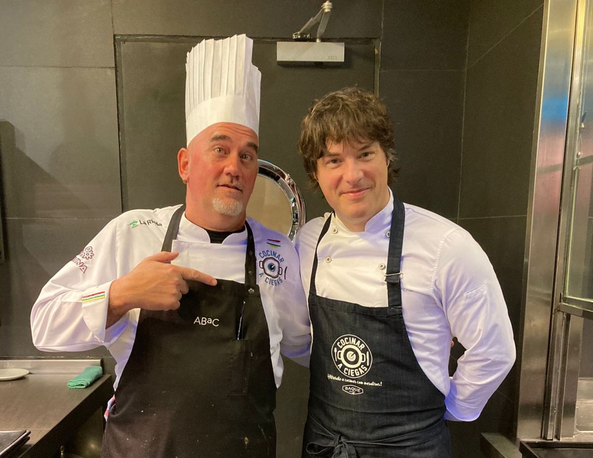 Ángel Palacios usando su uniforme de chef al lado de uno de sus alumnos quien mira sonriente.