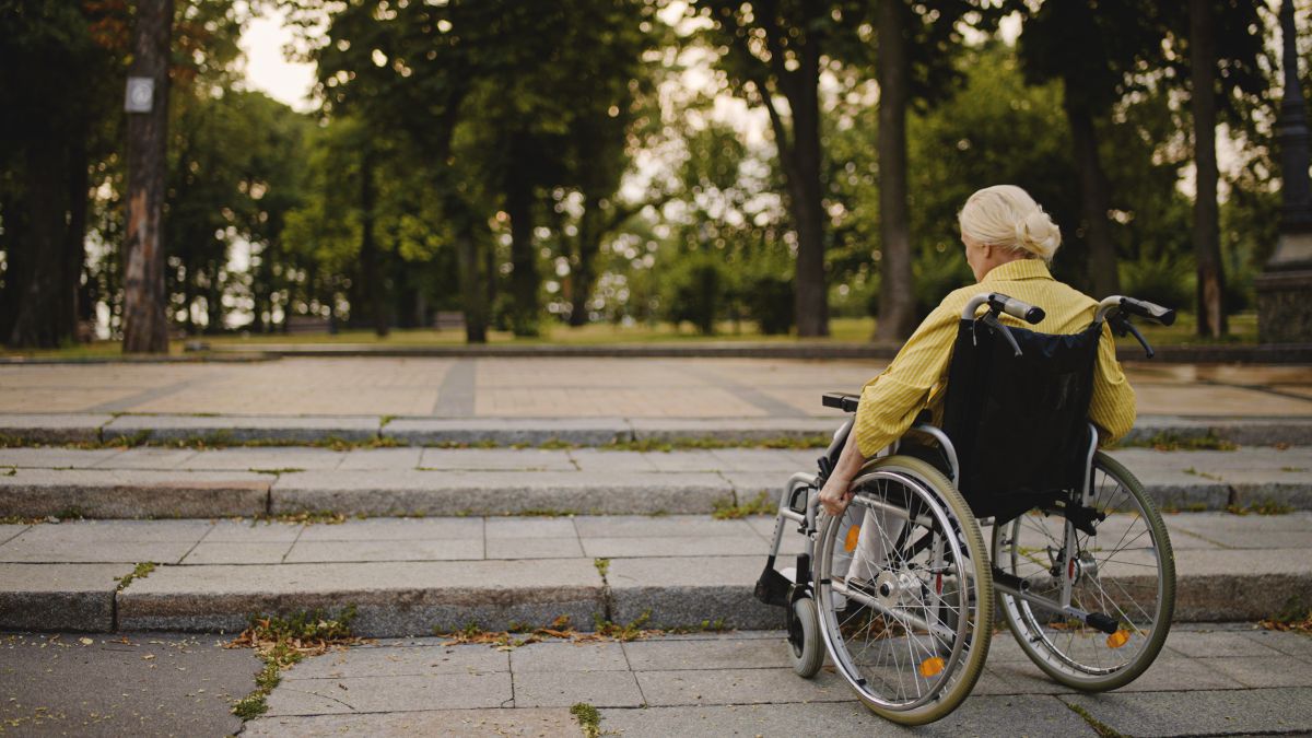 Una mujer en silla de ruedas frente a unos escalones sin rampa de acceso para pcd