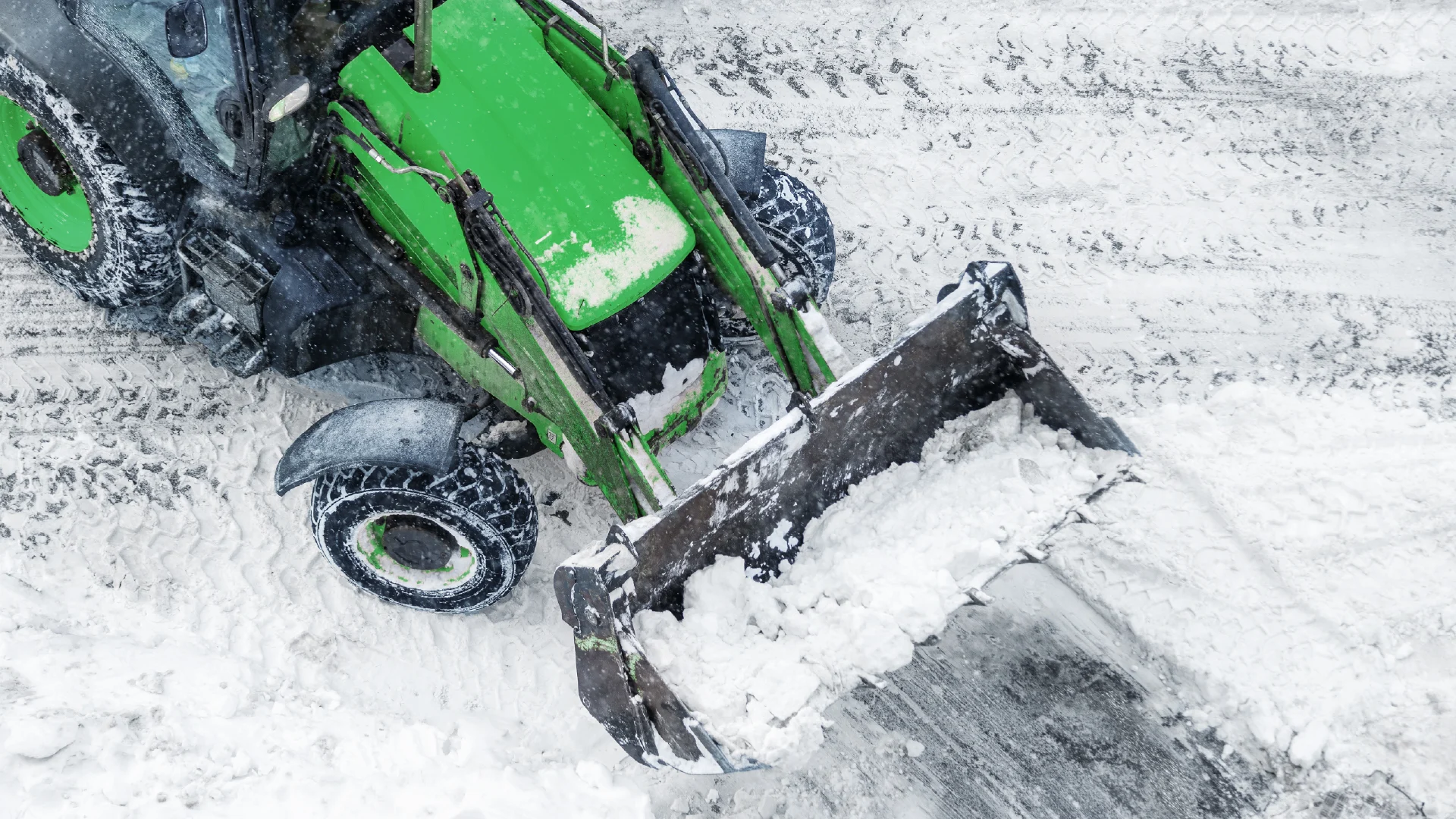 Vihreä pyöräkuormaaja kolaa lunta