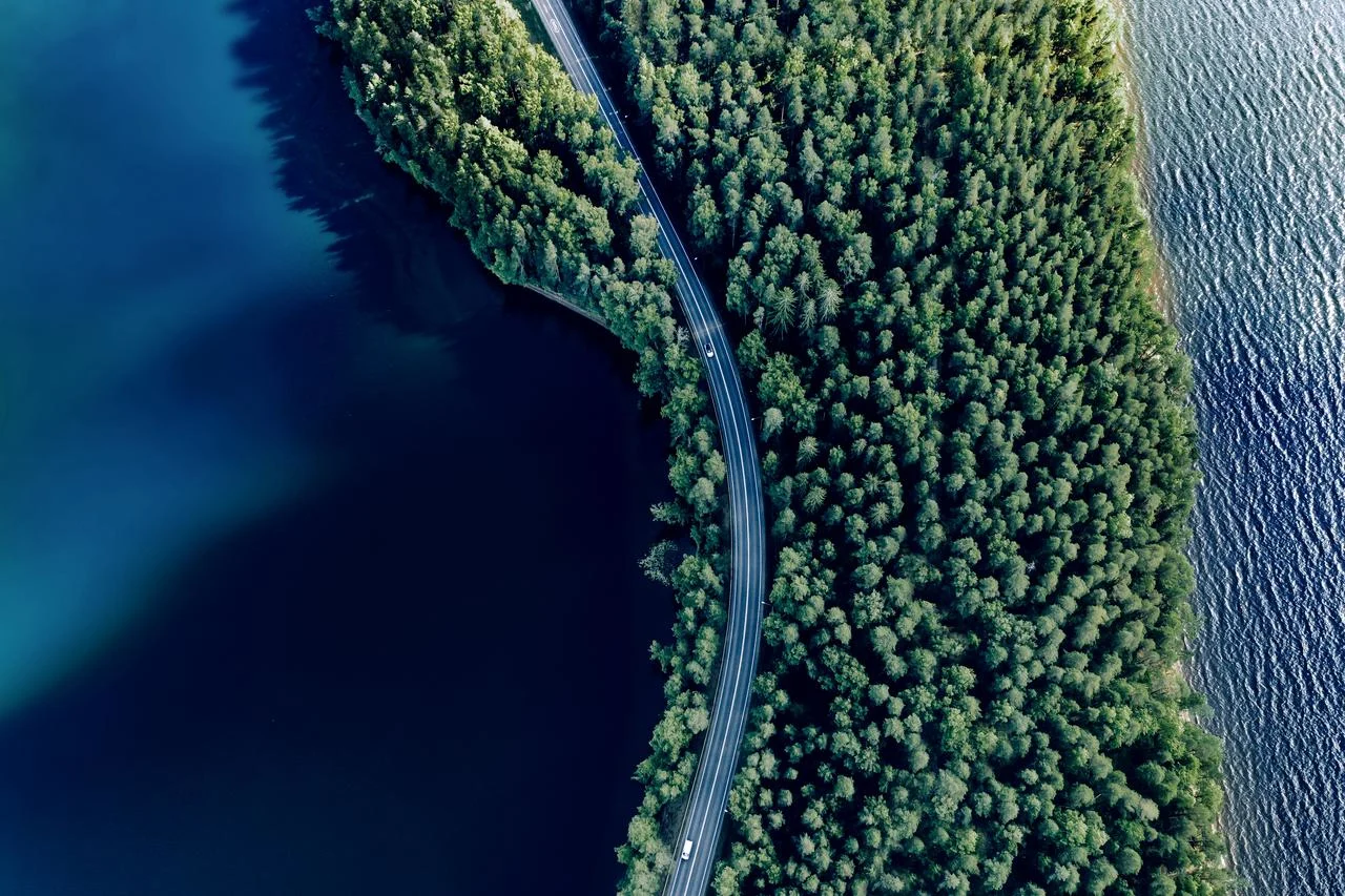 Aerial view of road in green woods and blue lakes water in summer Finland