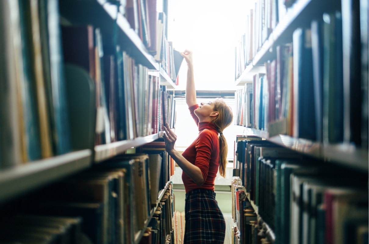 young teacher selects a book from a library shelf