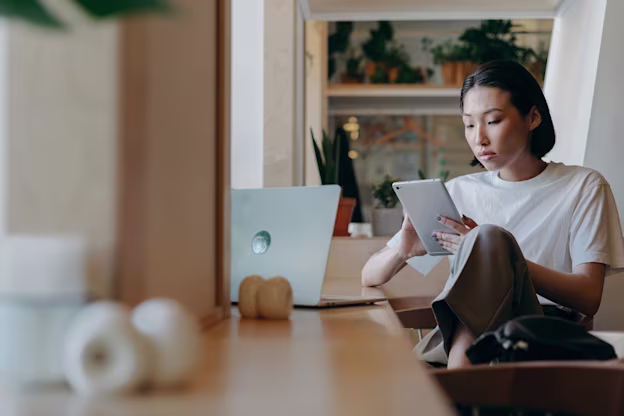 Woman Working on Laptop and Reading at Desk Indoors - stock image