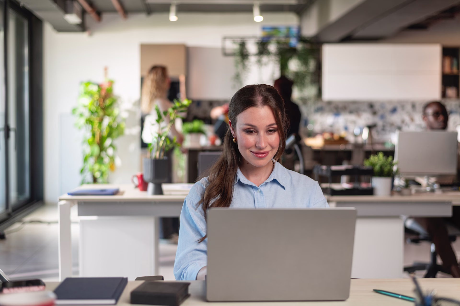 [visual] woman on laptop with plants and co workers in the background