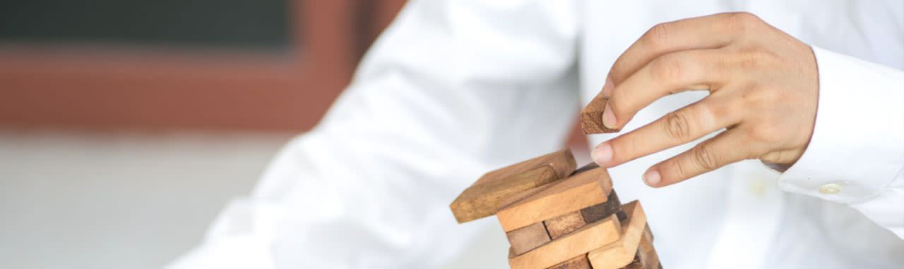 Un homme en chemise fait tombé une pyramide de morceau de bois