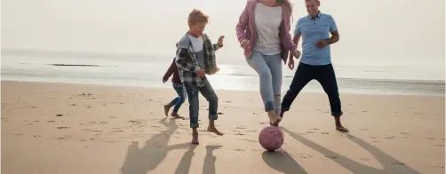Familie spiller fotball på stranden