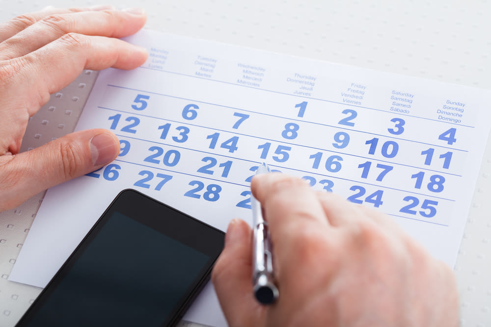 Close-up Of Hand Holding Pen Over Calendar With Mobile Phone