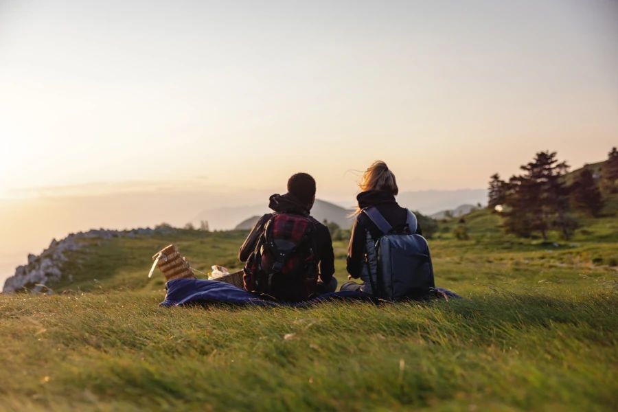 Un homme et une femme assis sur une colline, qui regardent un coucher de soleil.